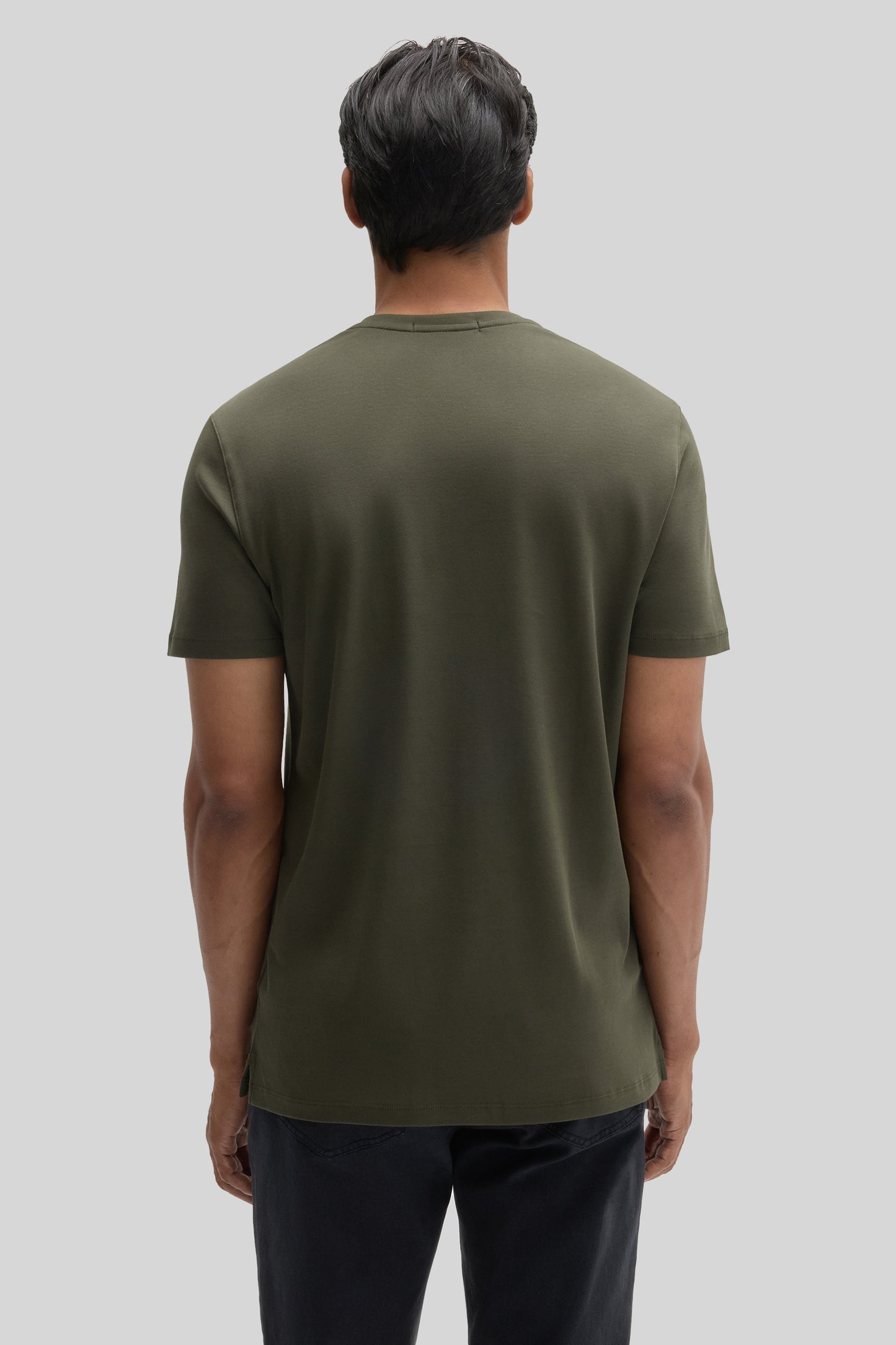 Man wearing olive green V-neck short-sleeve tee, back view, with dark pants.