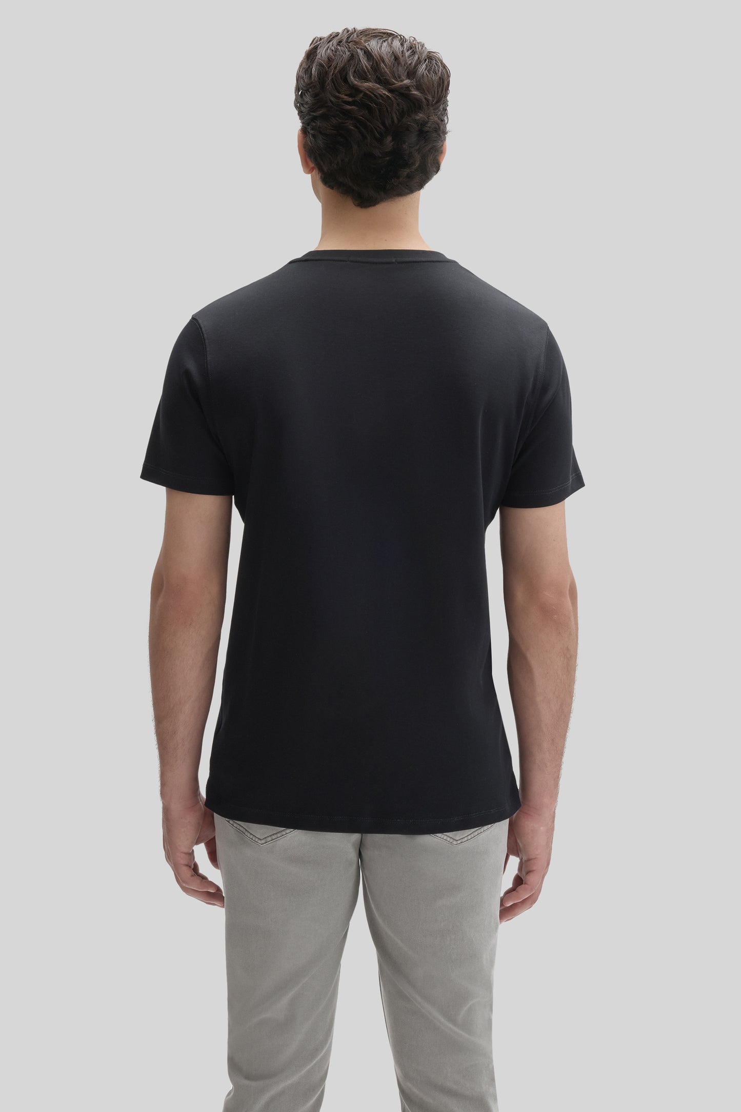 Man wearing black short-sleeve t-shirt and light gray pants, shown from back view.