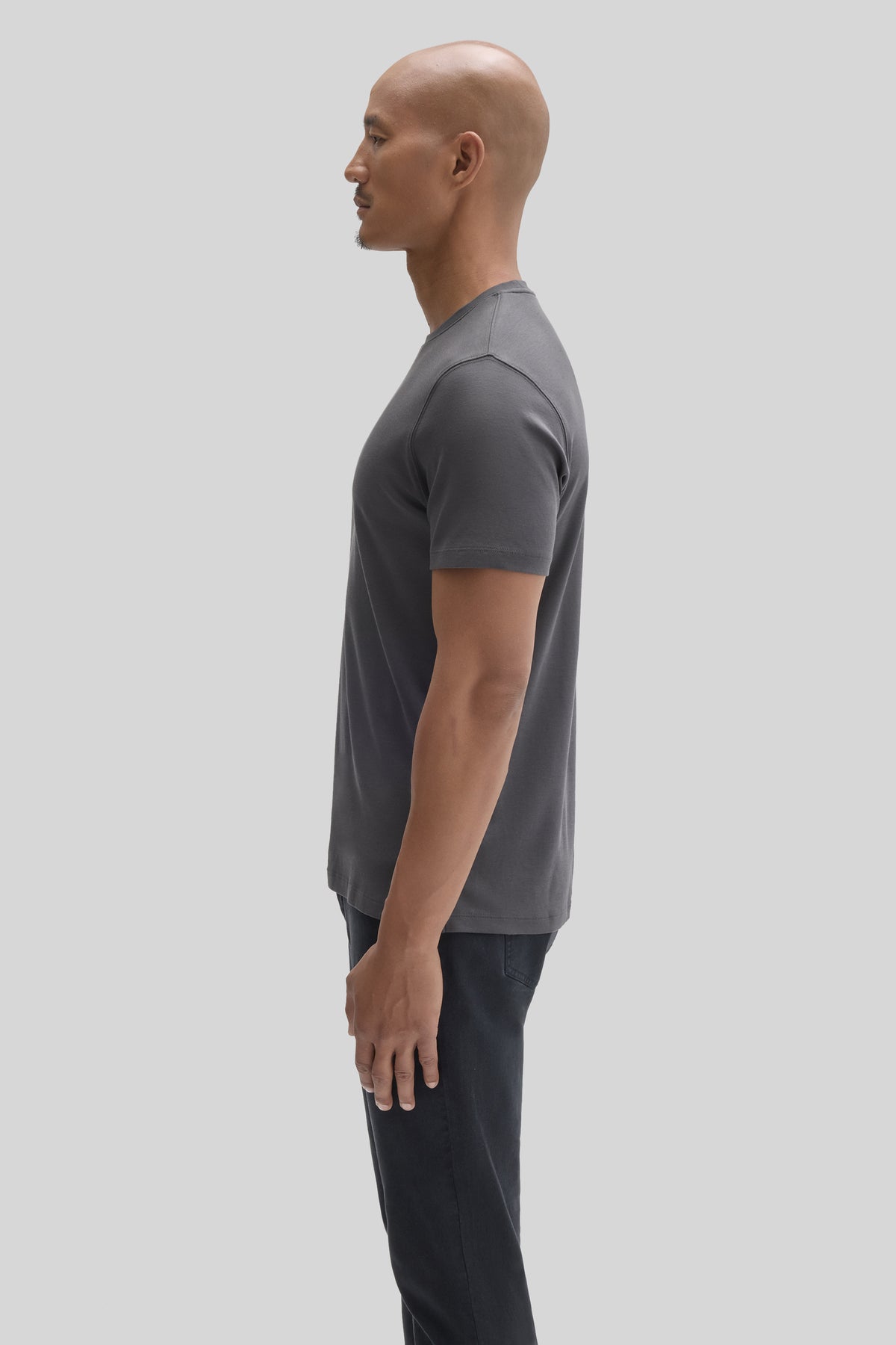 Man wearing a gray short-sleeve t-shirt and dark pants, shown in profile view.