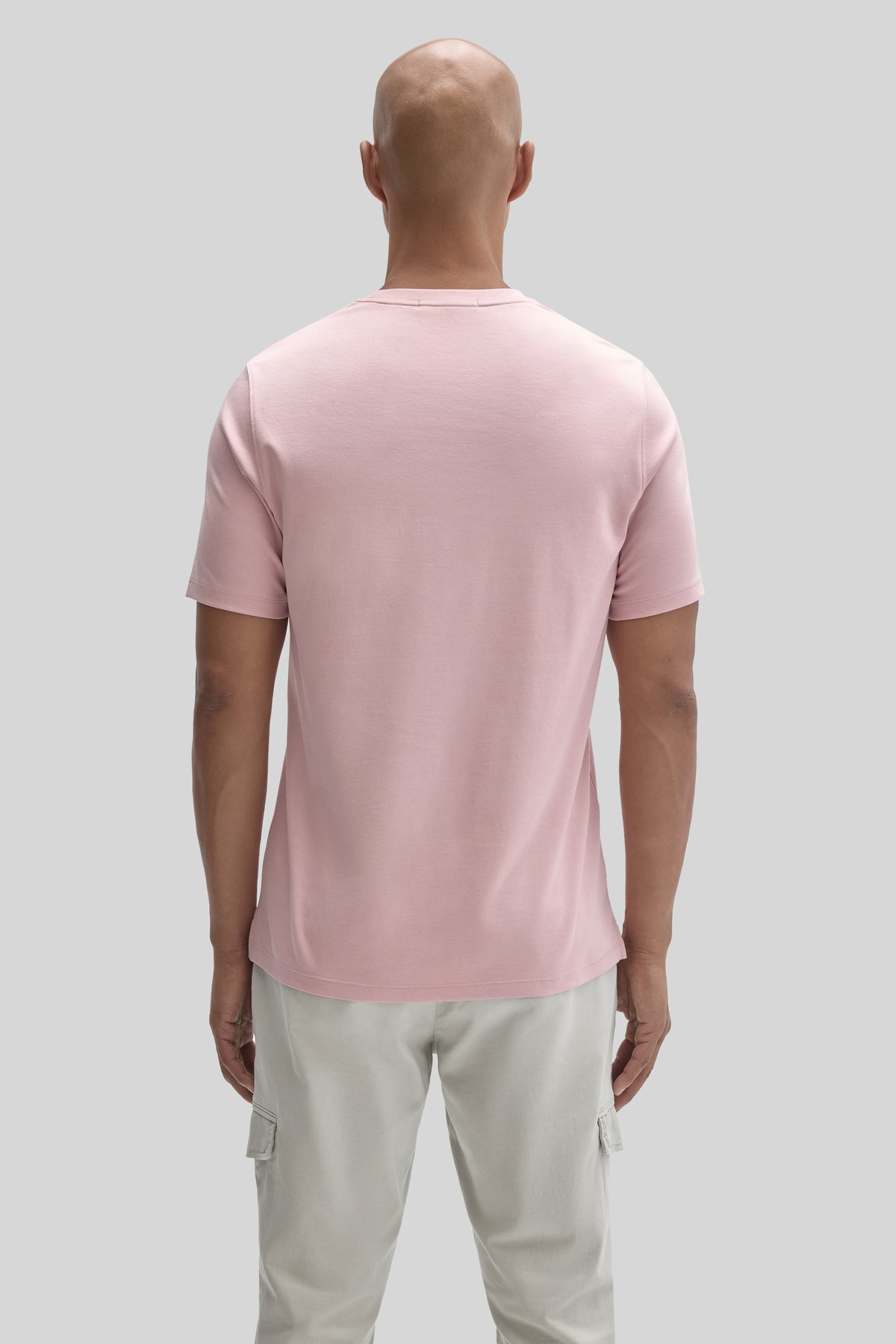 Man wearing light pink short-sleeve t-shirt and cream cargo pants, shown from back view.