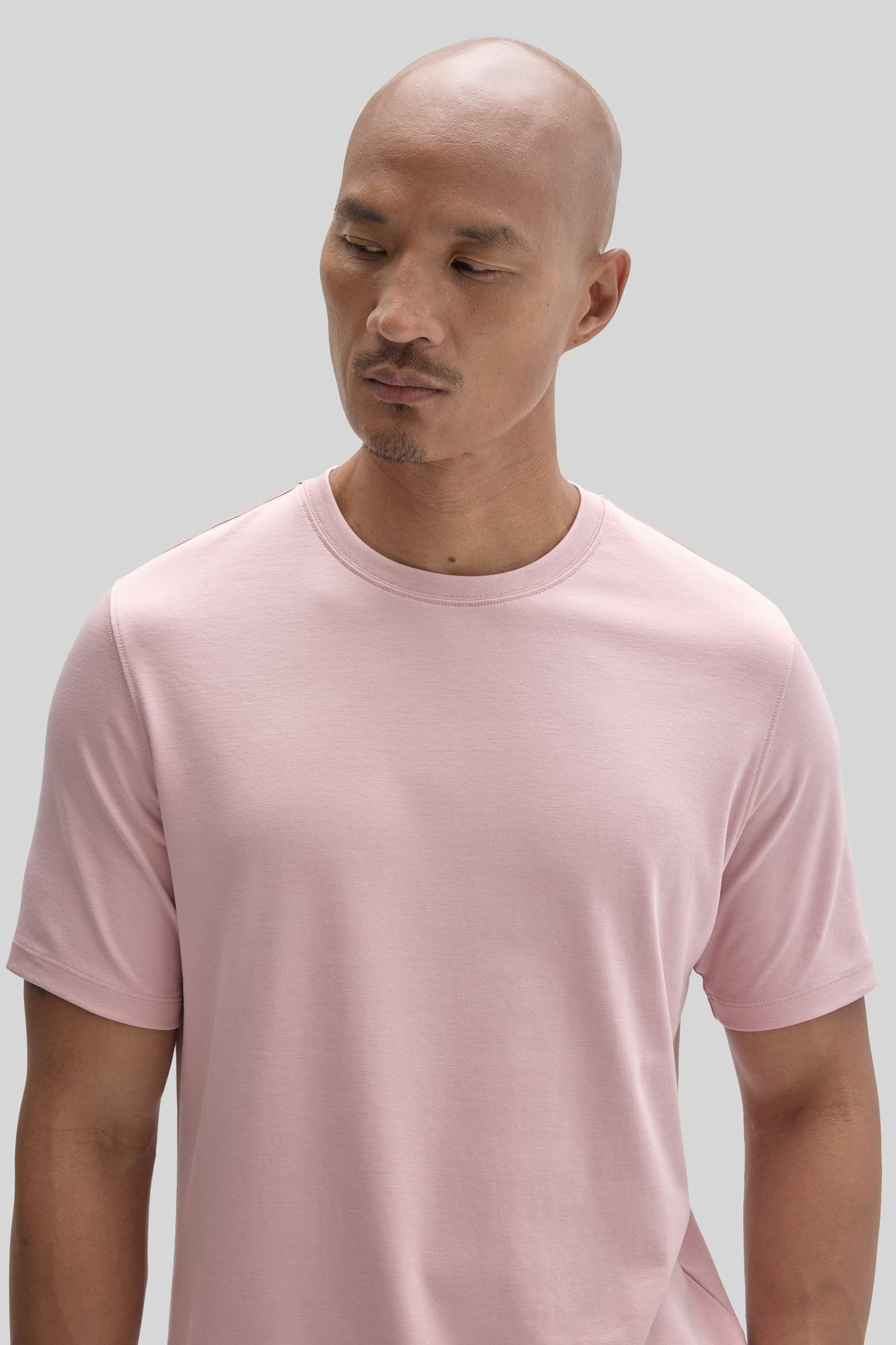 Man wearing a light pink crew-neck t-shirt with short sleeves against a neutral background.