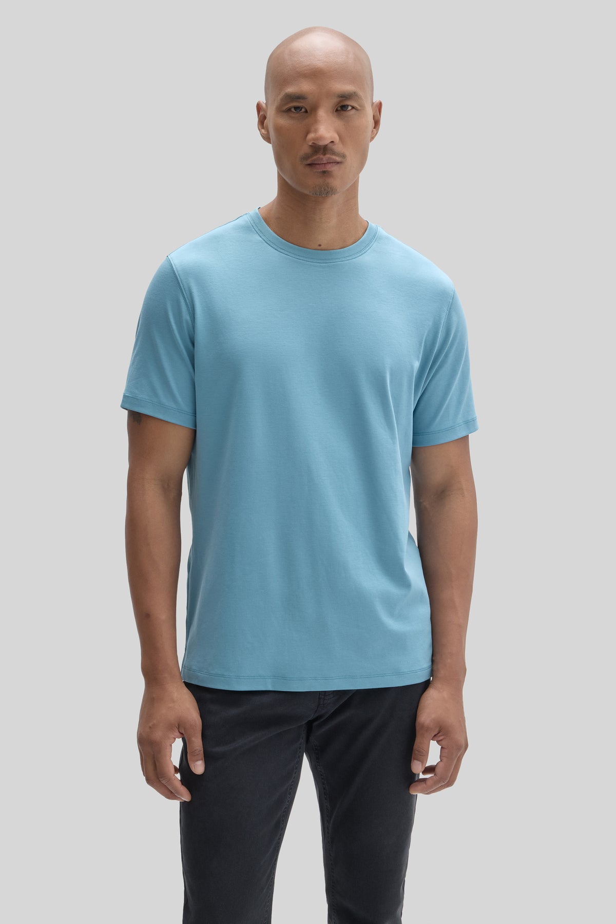 Man wearing a light blue crew neck t-shirt with short sleeves and black pants.