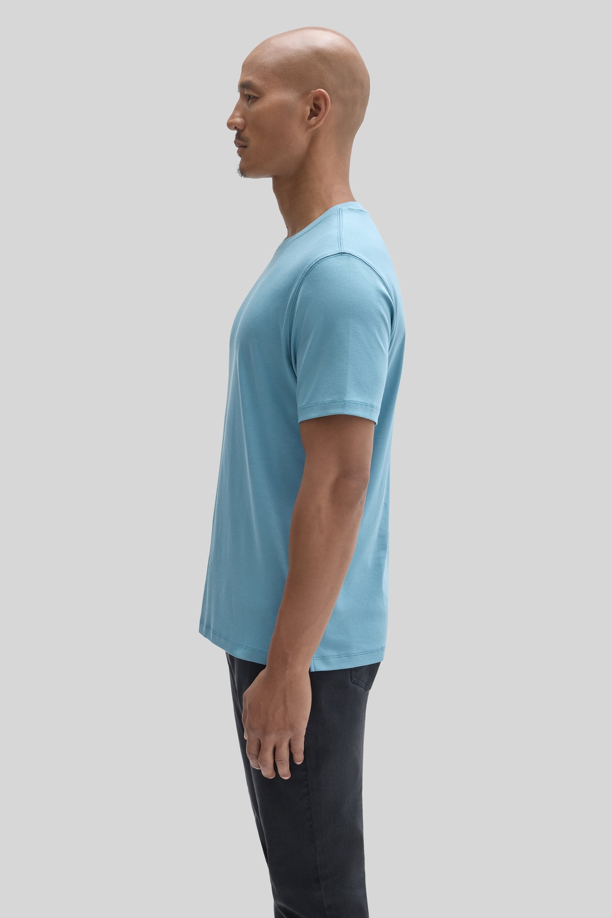 Light blue short-sleeve t-shirt on male model wearing dark pants, side profile view.
