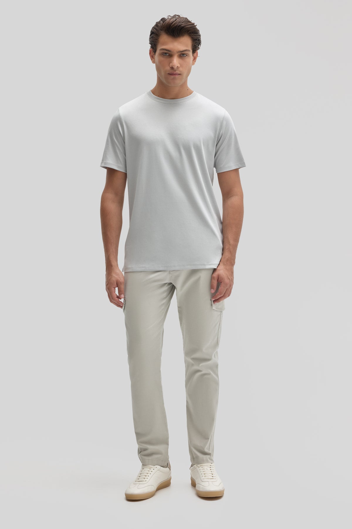 Man wearing light gray crew neck t-shirt with beige cargo pants and cream sneakers.