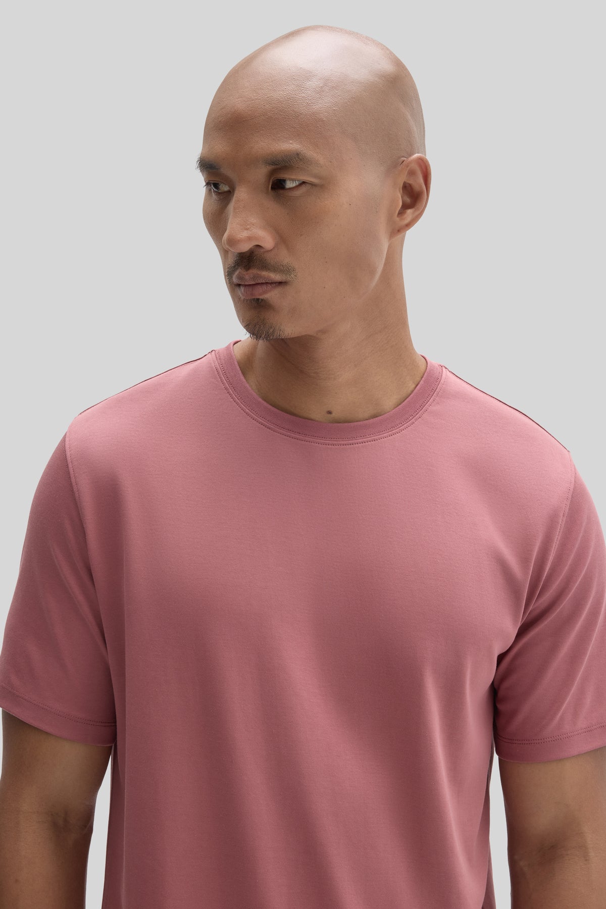 Man wearing a rose pink crew neck t-shirt with short sleeves against a gray background.
