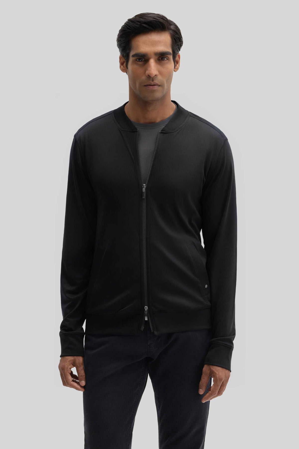 Man wearing black baseball jacket with full-length zip and ribbed cuffs over dark pants.