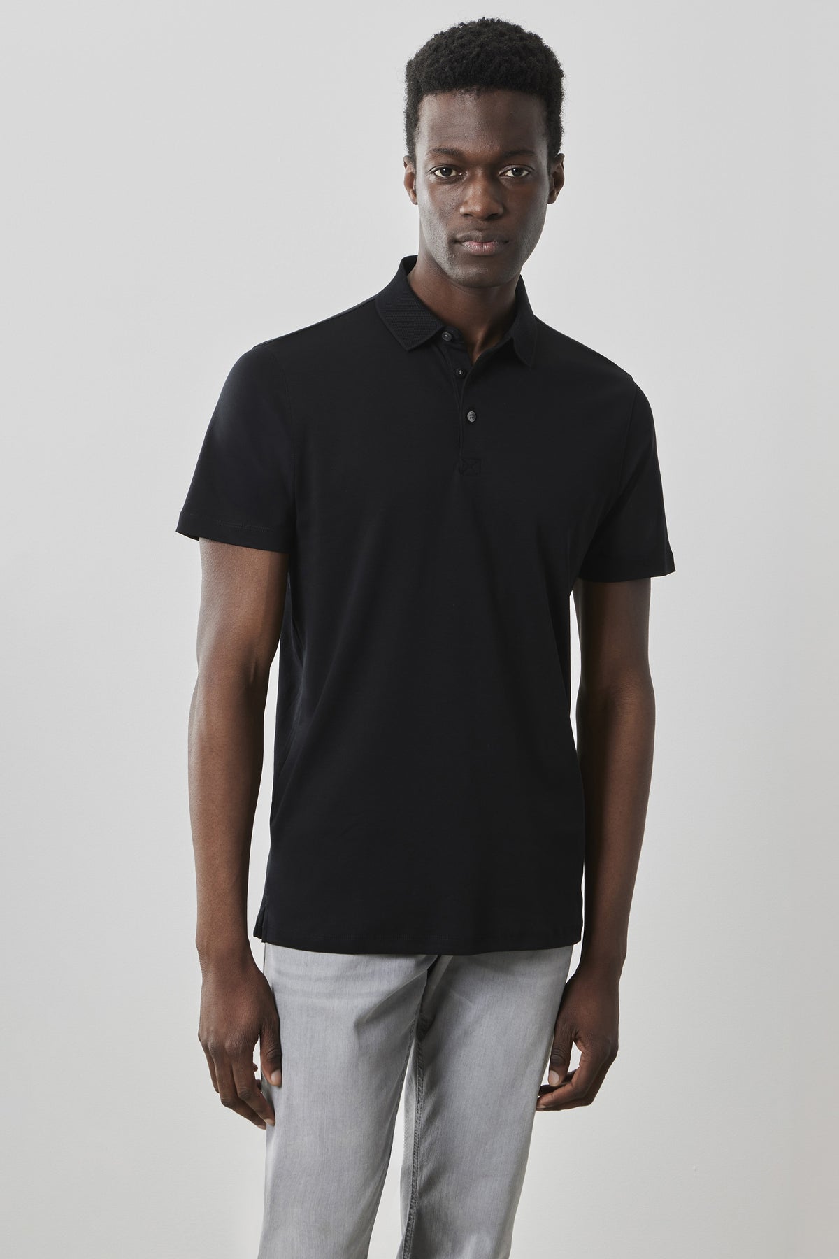 Man wearing black short-sleeve polo shirt with collar and buttons, paired with light gray pants.