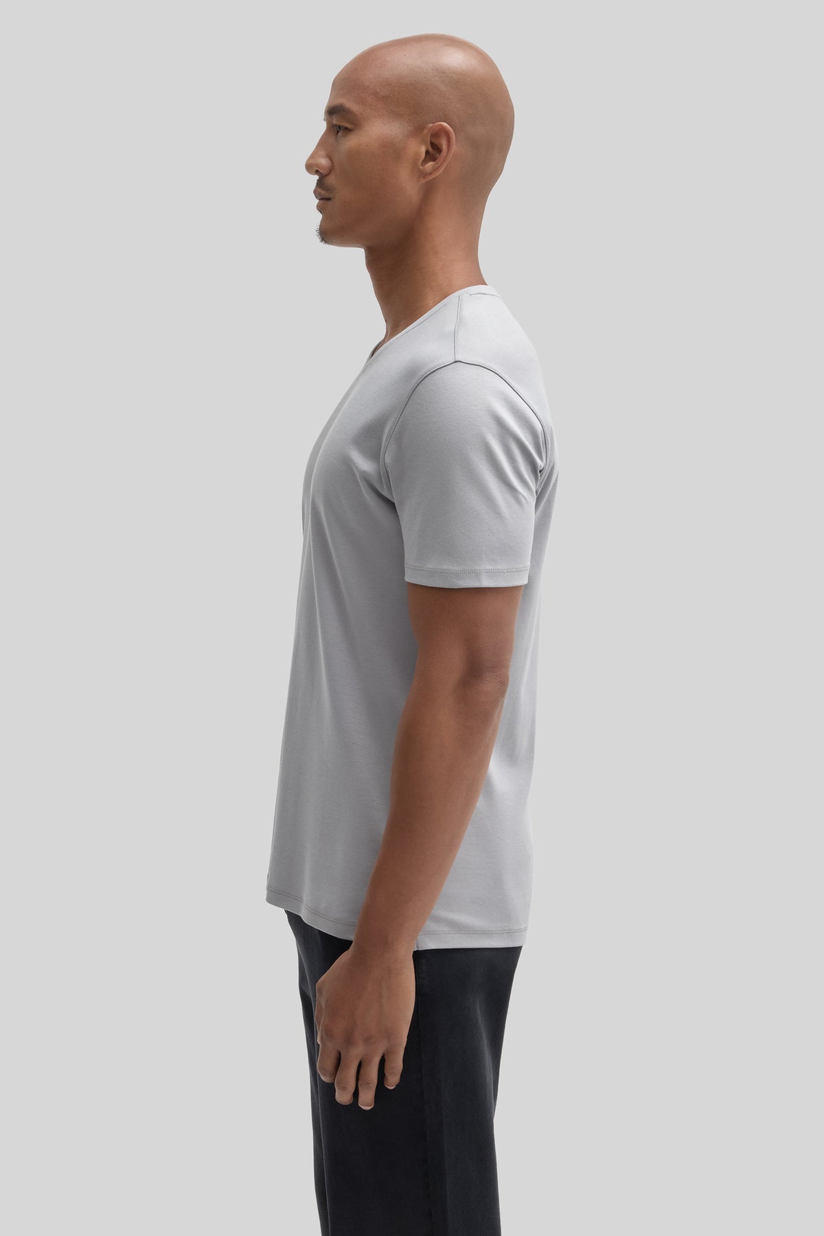 Man wearing light gray V-neck t-shirt with black pants, shown from side profile.