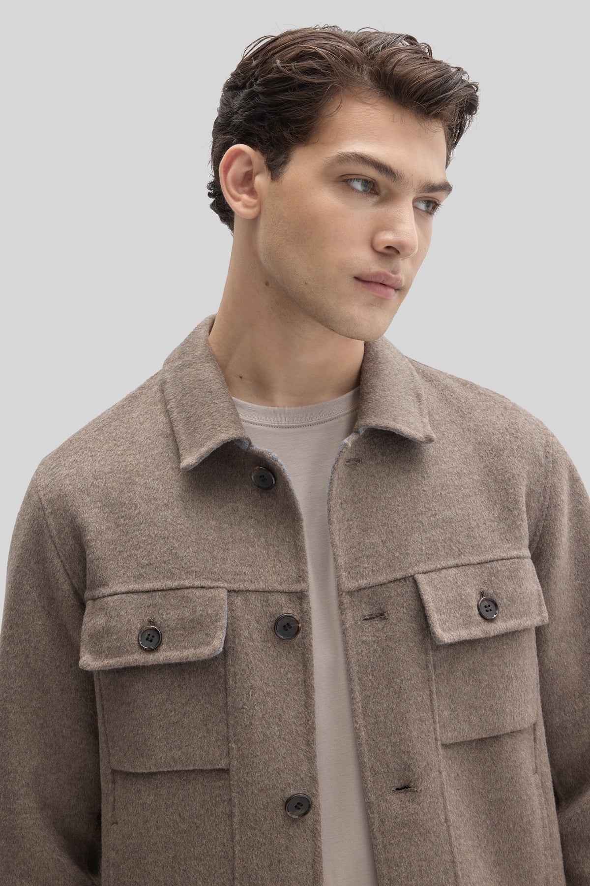 Man wearing a beige buttoned jacket with chest pockets and collar over a cream-colored shirt.