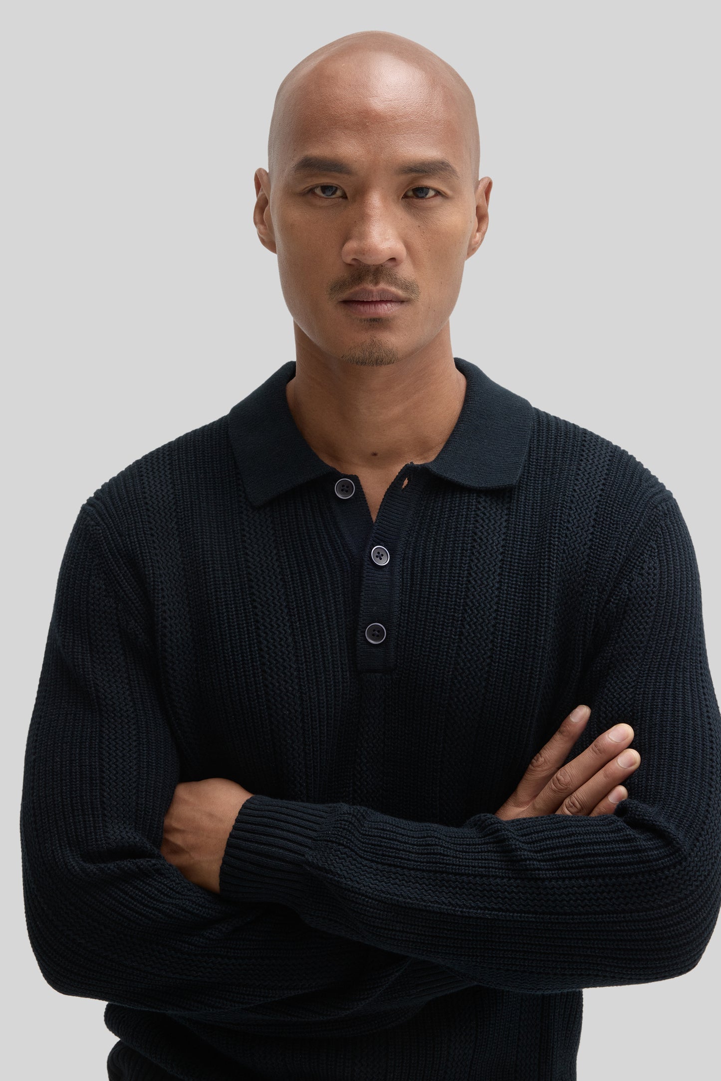 Man wearing black sweater polo with textured knit fabric and button placket at neckline.