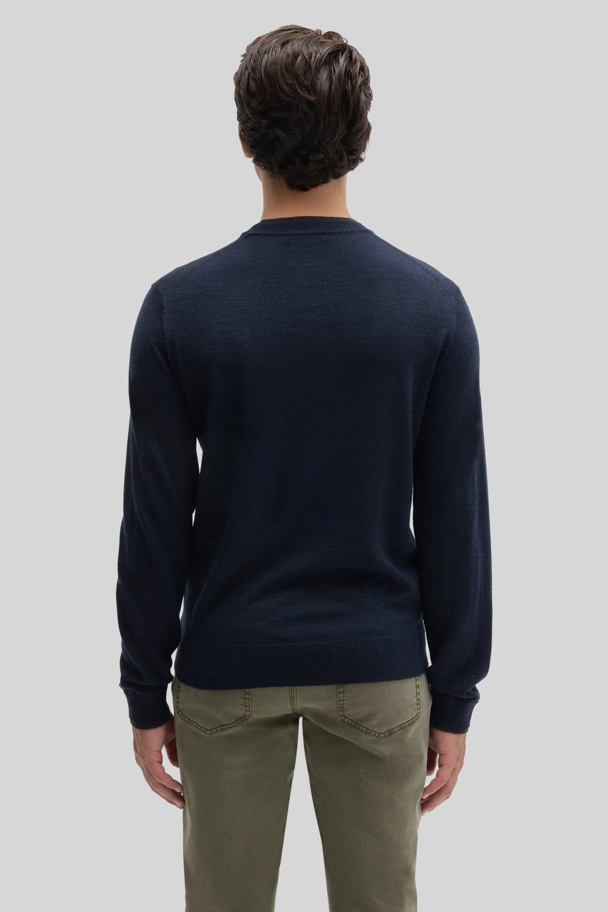 Navy crewneck sweater with long sleeves worn with khaki pants, shown from back view.