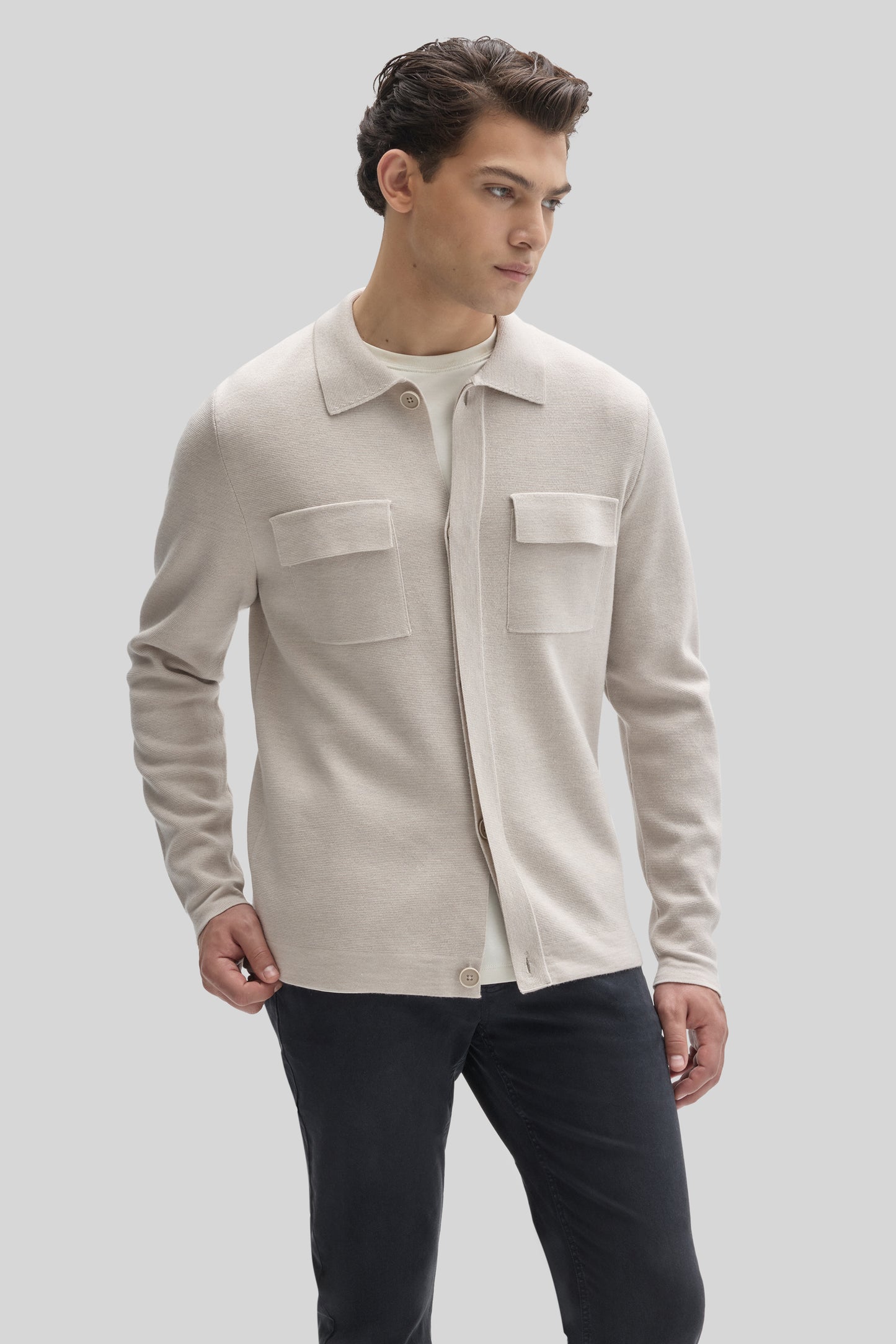 Beige buttoned cardigan with collared neckline and chest pockets worn over a white shirt with dark trousers.