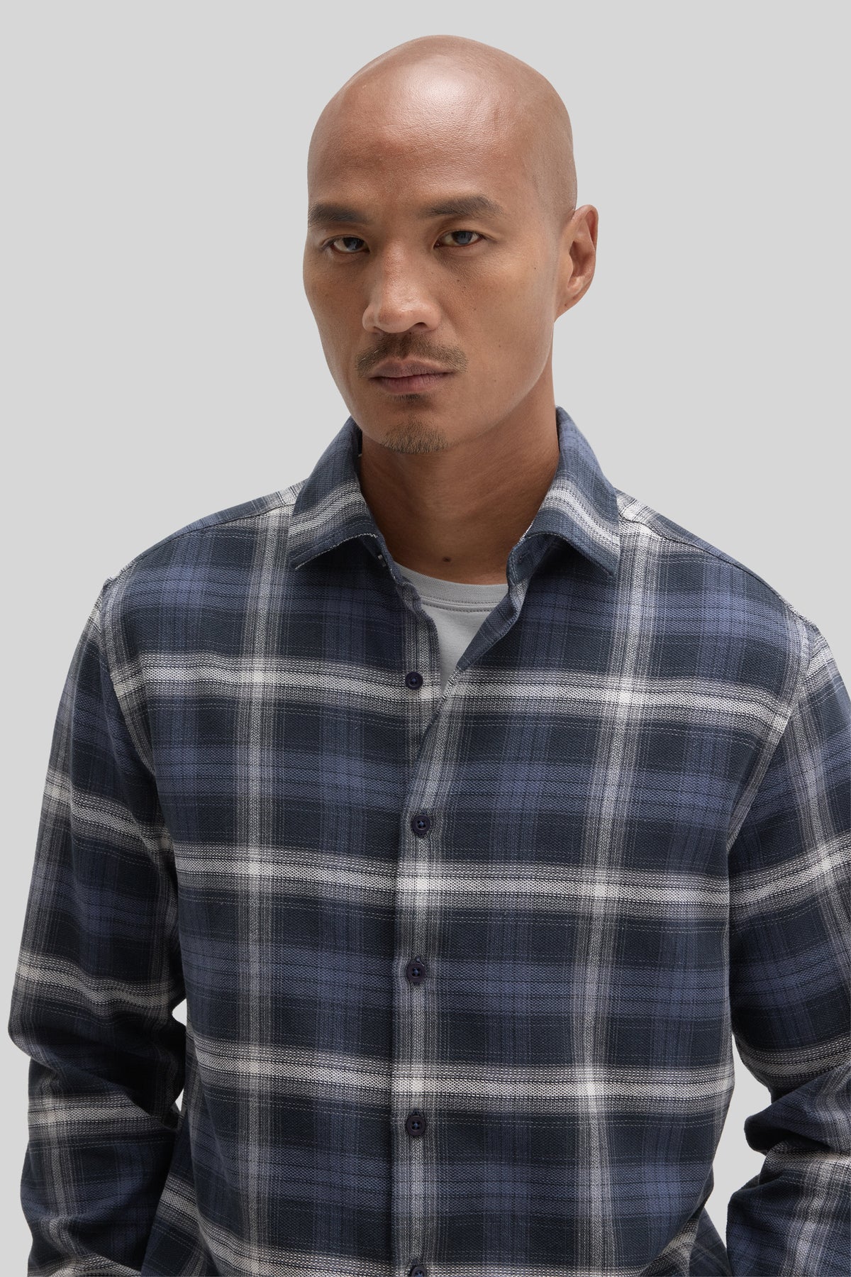 Man wearing navy and white plaid corduroy woven shirt with button front over gray undershirt.