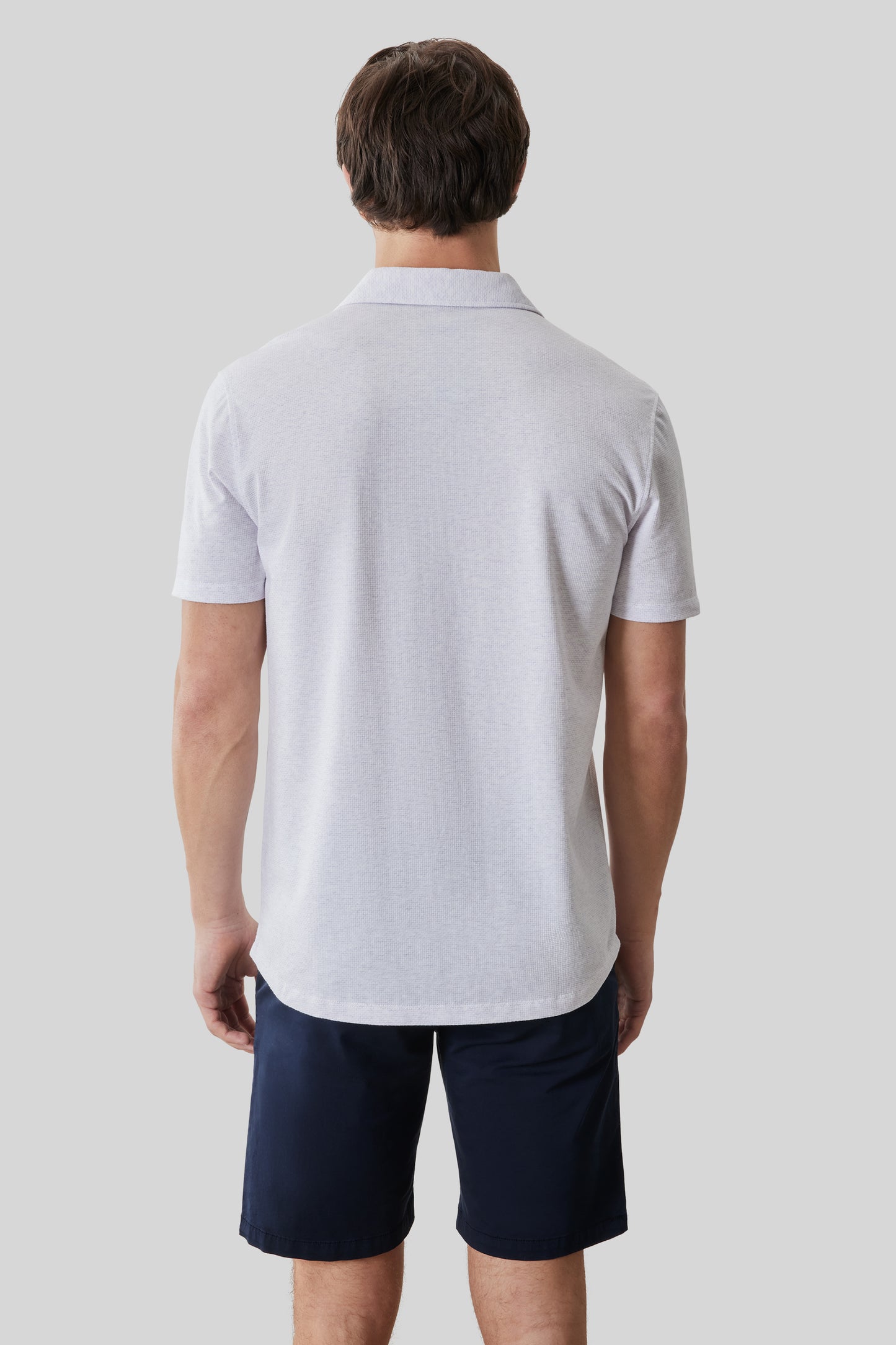 Man wearing light gray short-sleeve knit shirt with collar, shown from back, paired with navy shorts.