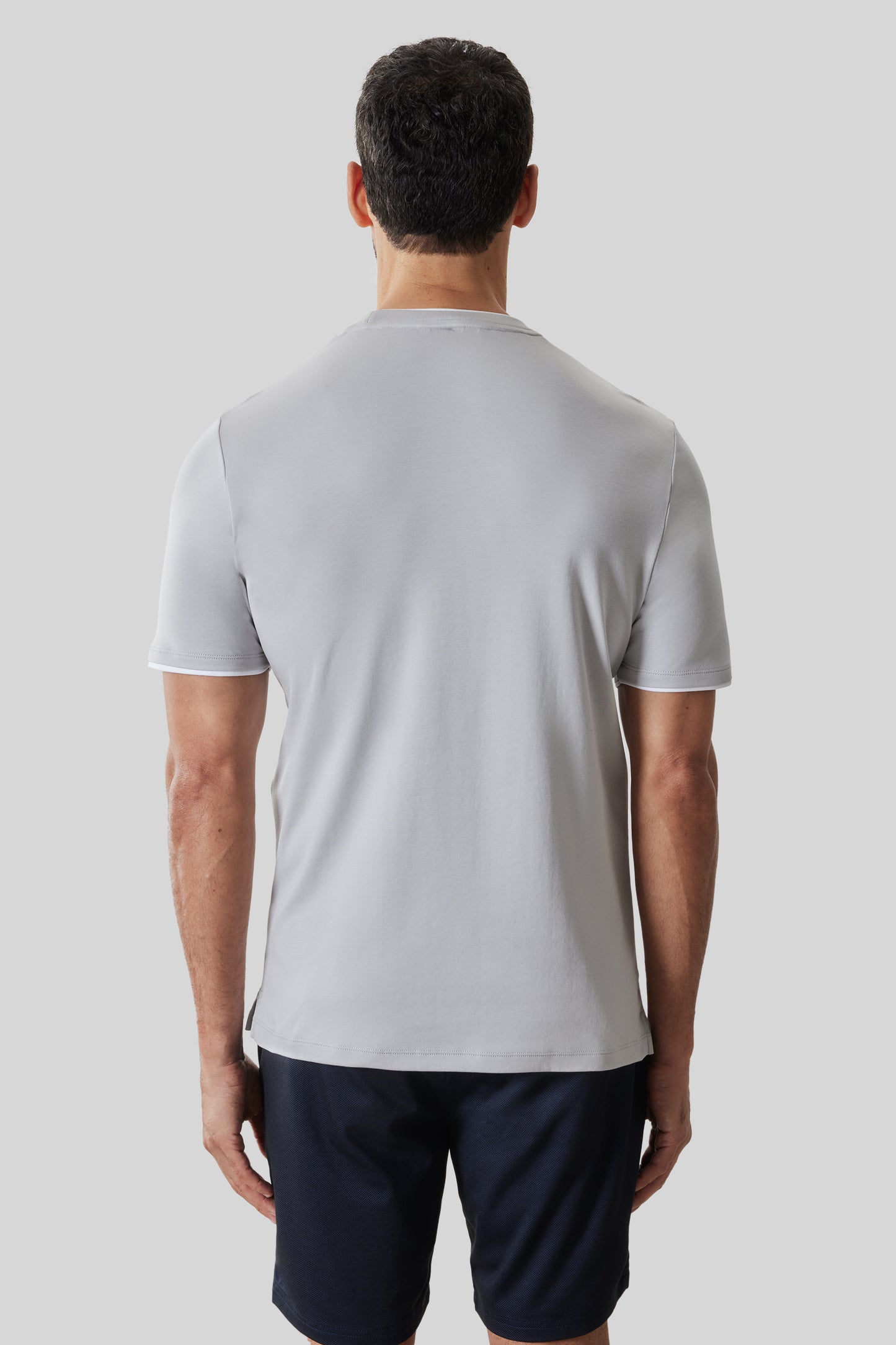 Man wearing light gray short-sleeve tee with white collar trim and dark navy shorts, viewed from behind.