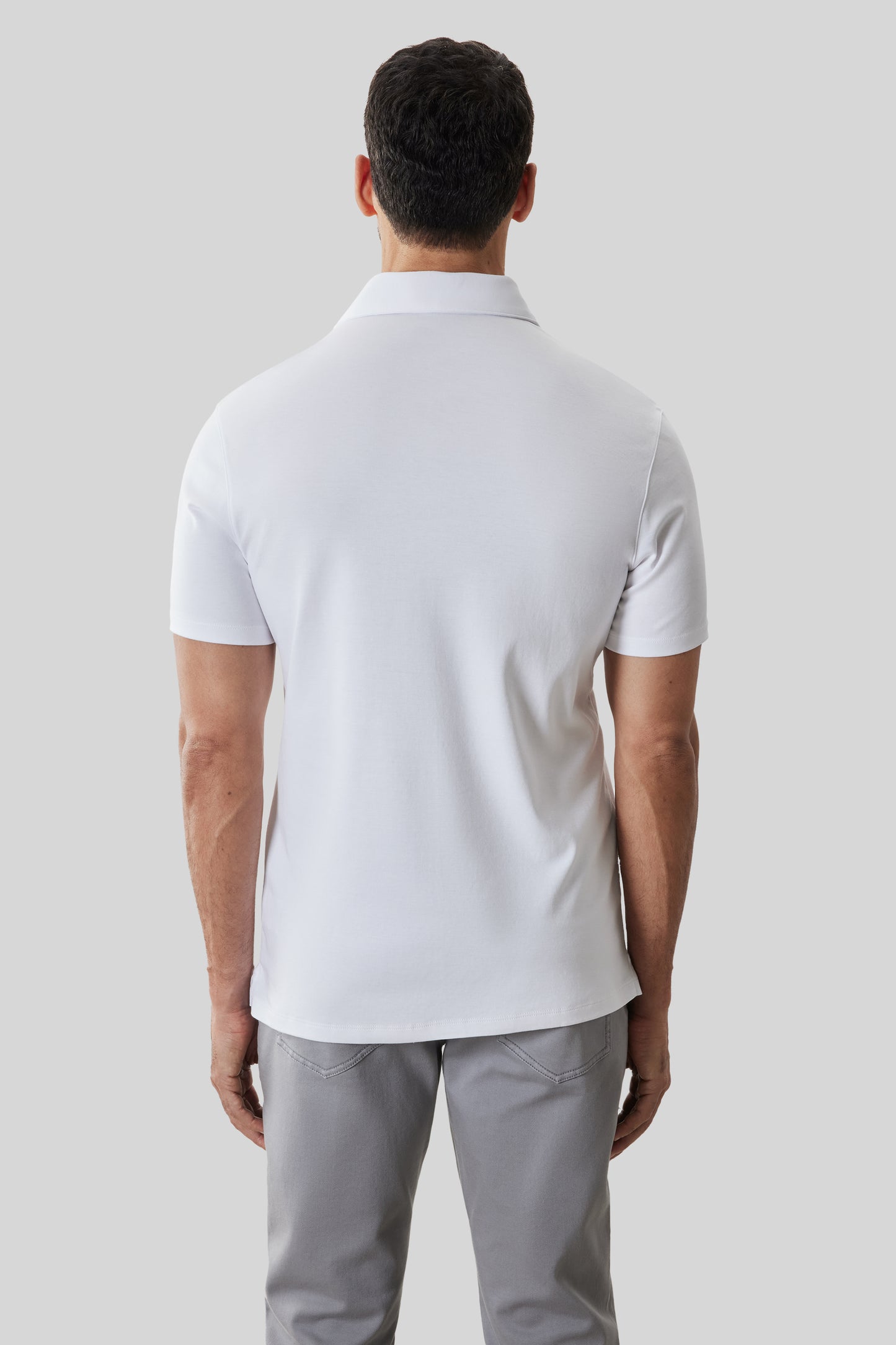 White short-sleeve polo shirt with collar, shown from back view on model wearing gray pants.