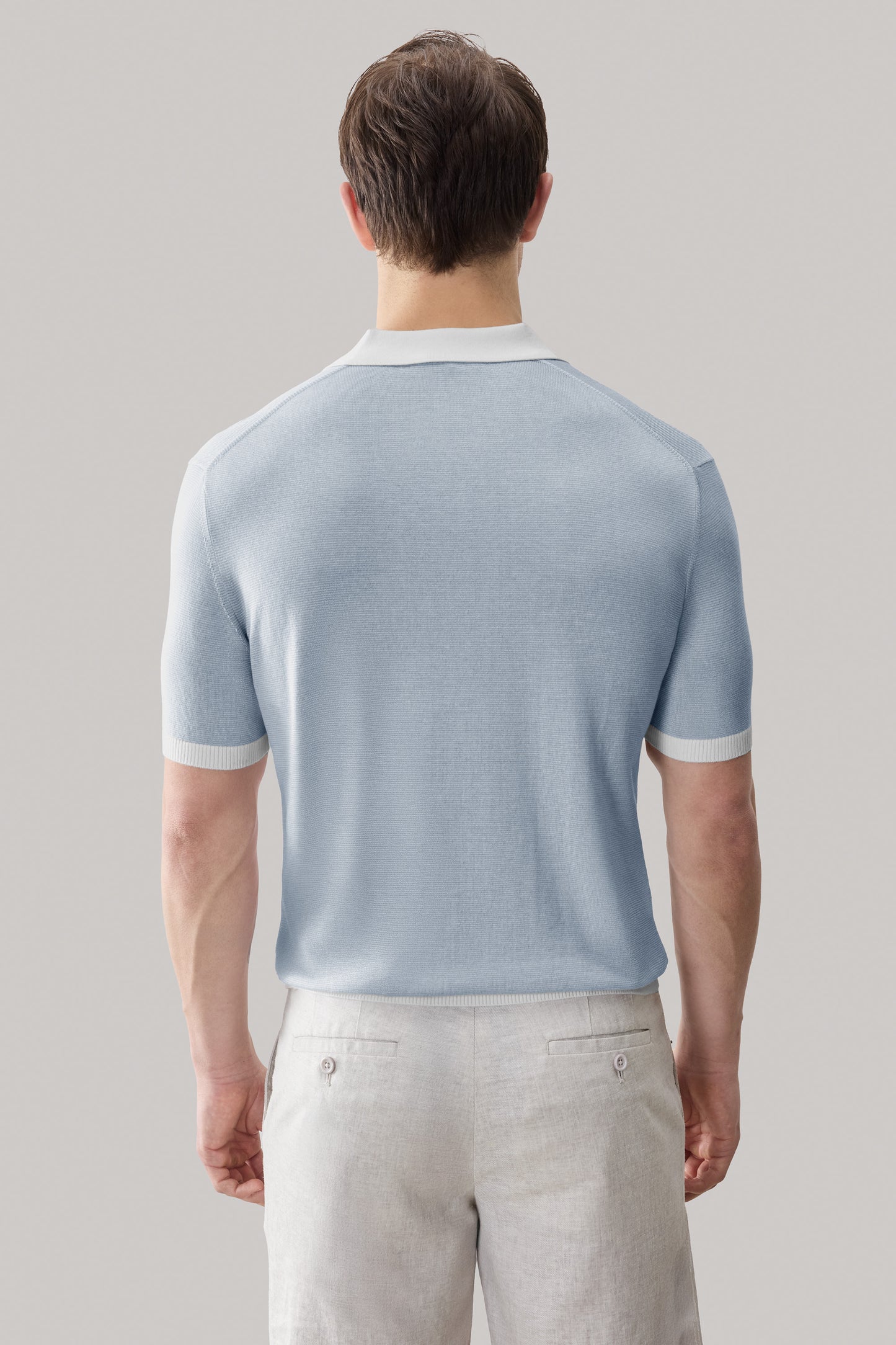 Light blue short-sleeve sweater polo with white collar and cuff trim, worn with cream trousers.