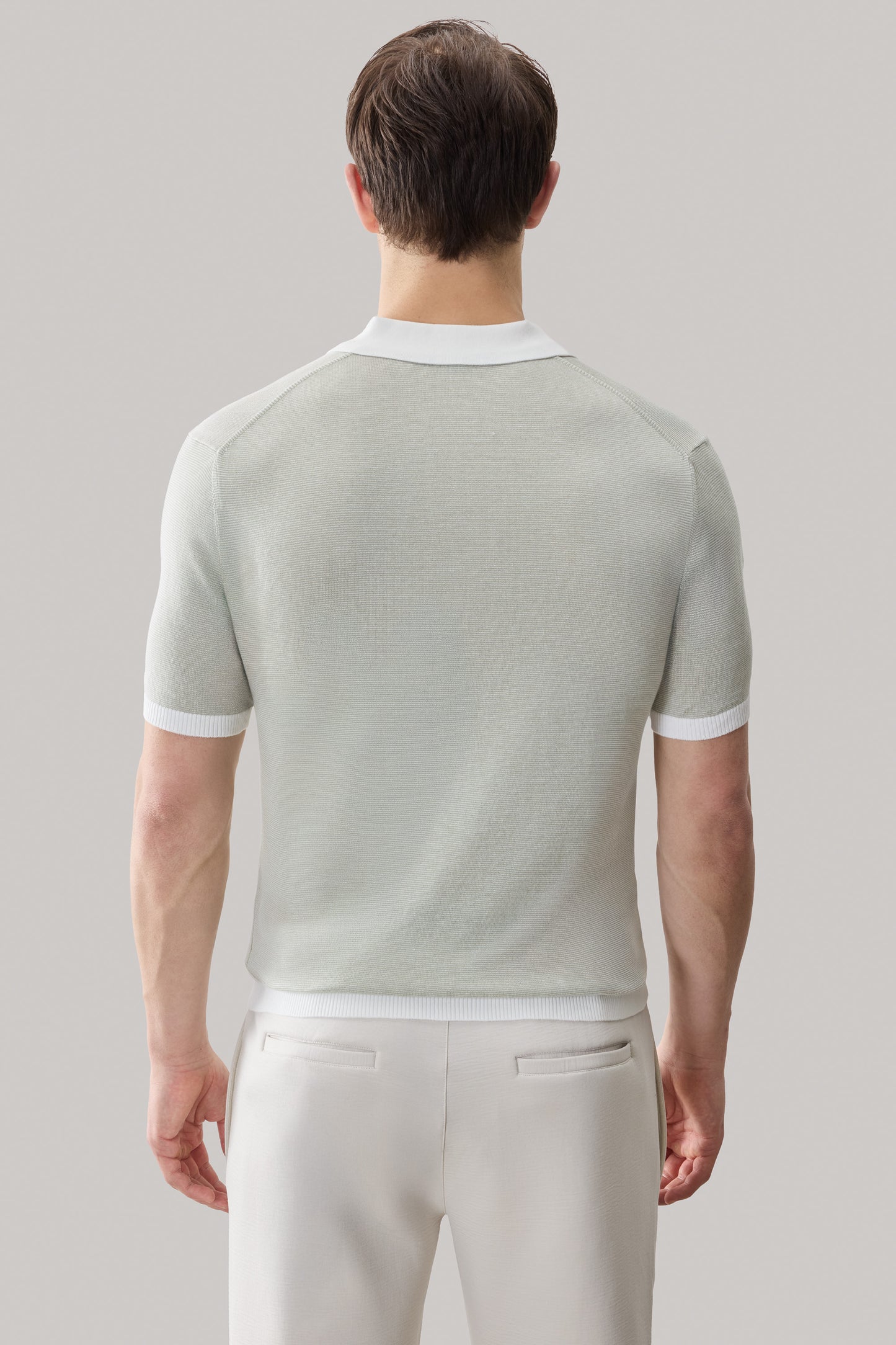 Man wearing light gray sweater polo with white collar and sleeve stripes, shown from back.