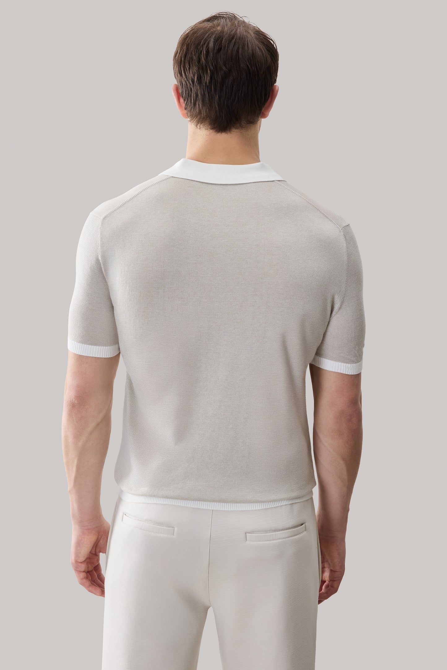 Beige sweater polo with white collar and ribbed trim on sleeves, shown from back on model wearing cream pants.
