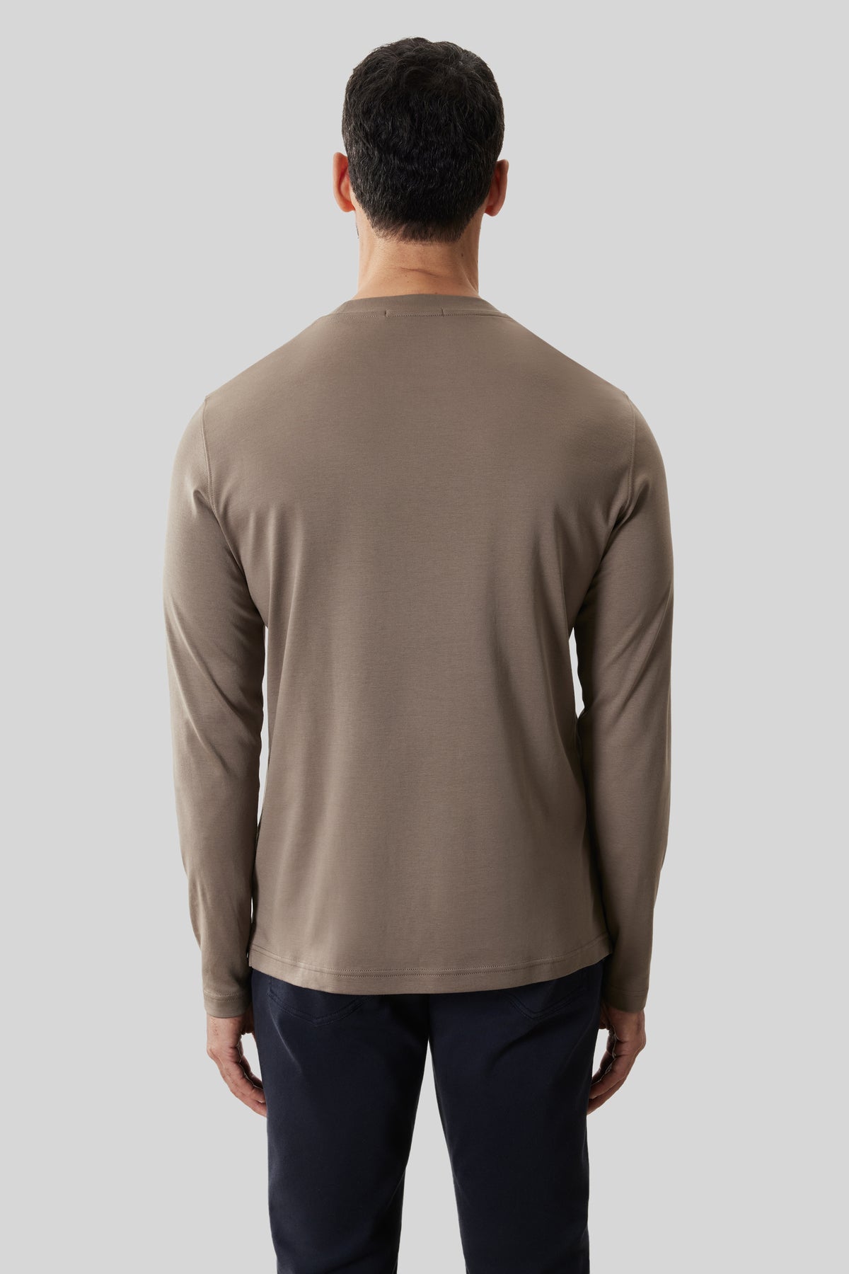 Man wearing taupe long-sleeve crew neck shirt with dark navy pants, shown from behind.