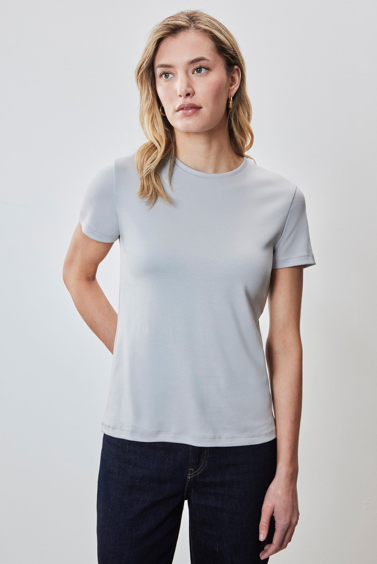 Woman wearing light gray short-sleeve crewneck tee with dark denim jeans.