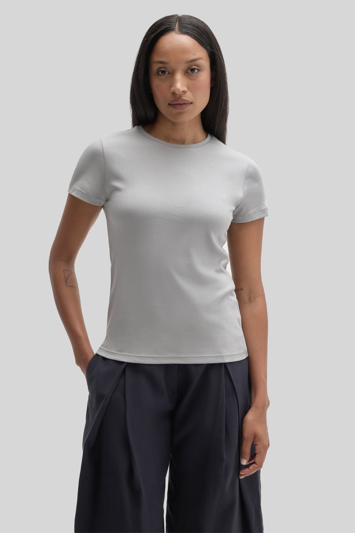 Woman wearing a light gray short-sleeve crewneck tee with navy trousers.