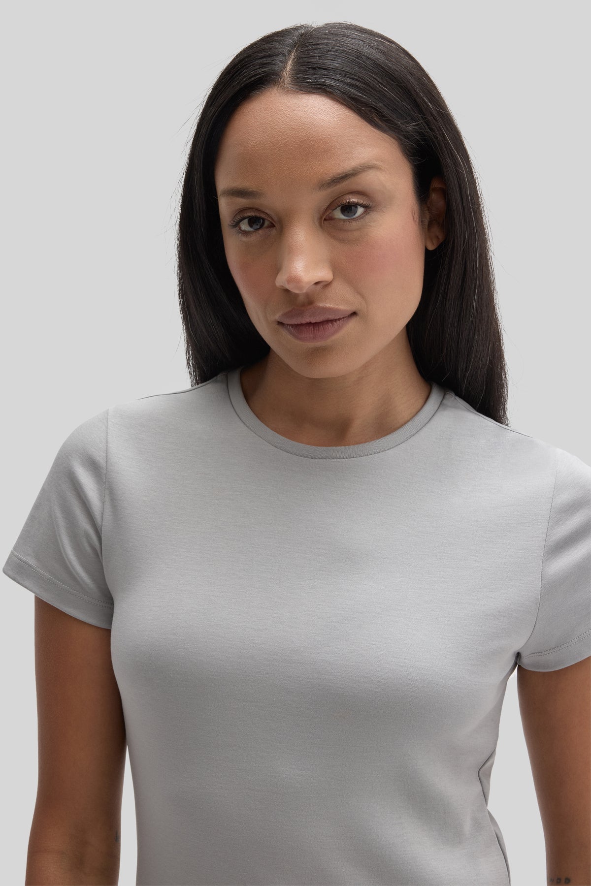 Woman wearing a light gray short-sleeve crew neck t-shirt against a neutral background.