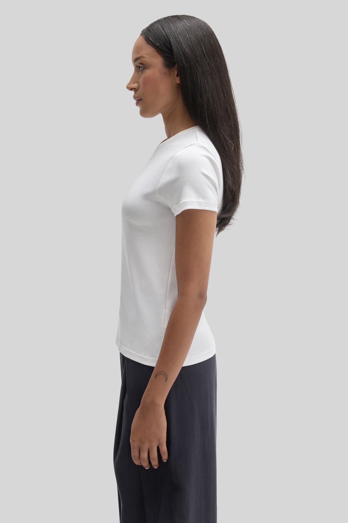 Woman wearing white short-sleeve crew neck tee with black pants, shown in profile view.