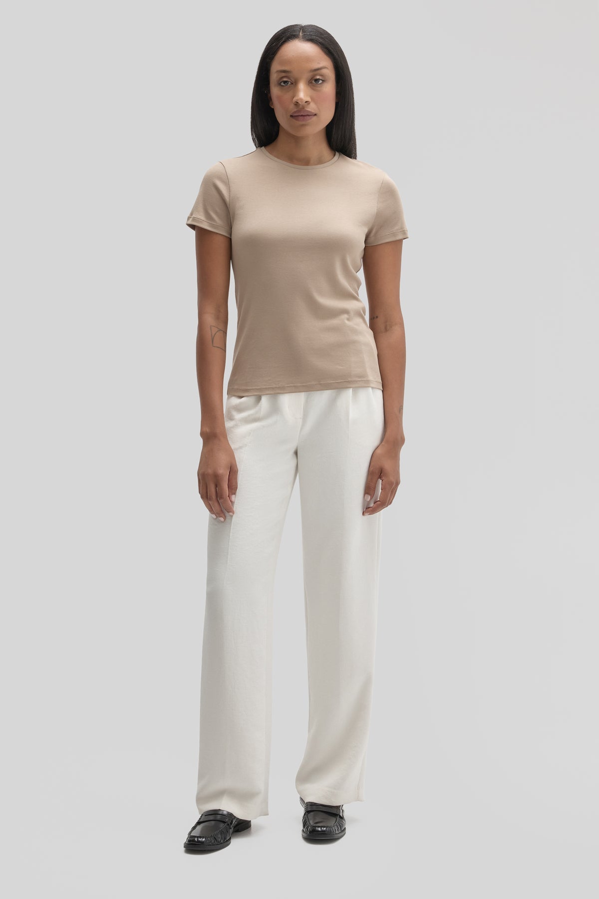 Woman wearing a beige short-sleeve crewneck tee with white wide-leg pants and black slide sandals.