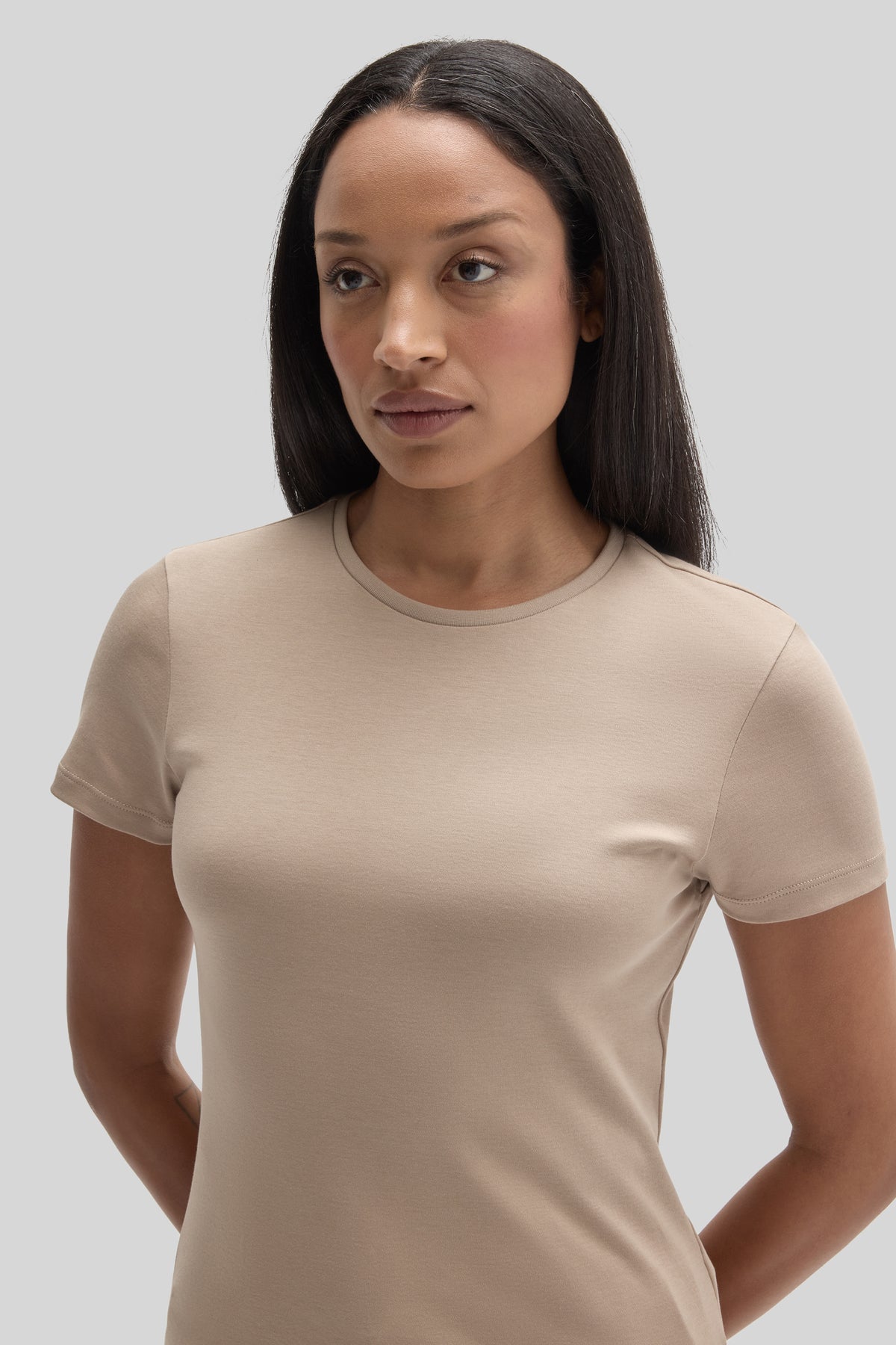 Woman wearing a beige crew neck short-sleeve t-shirt against a neutral background.
