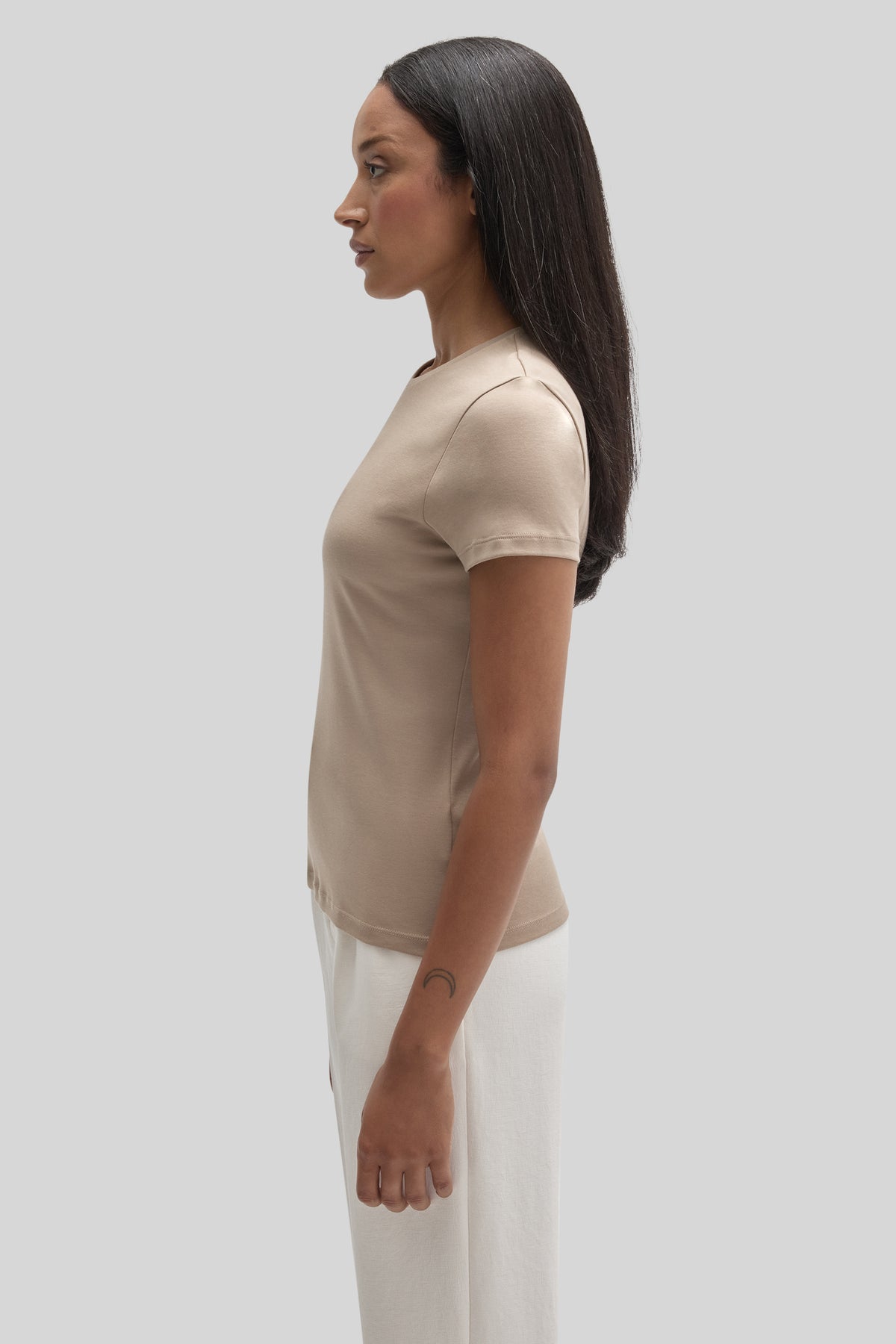 Woman wearing a beige short-sleeve crew neck tee, shown in profile view against a neutral background.