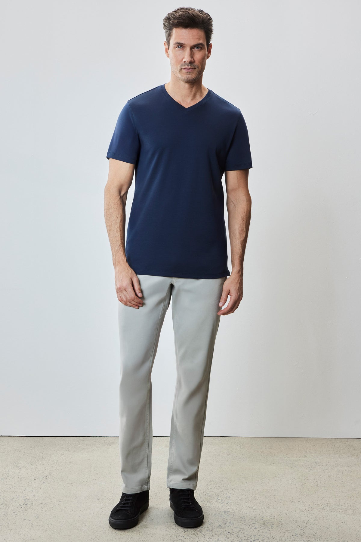 Man wearing navy blue V-neck short-sleeve t-shirt with light gray pants and black shoes.