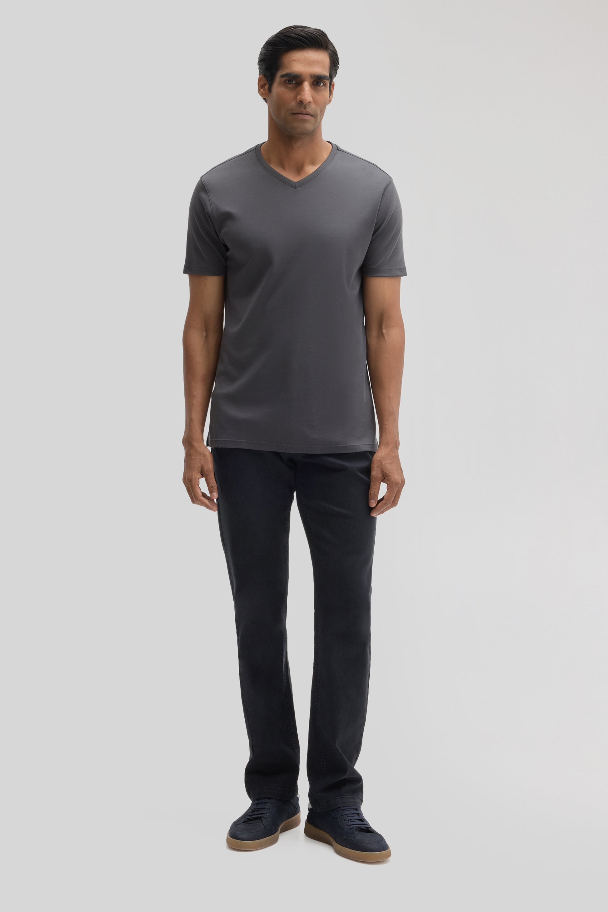 Man wearing charcoal V-neck t-shirt with short sleeves, black pants, and navy sneakers.
