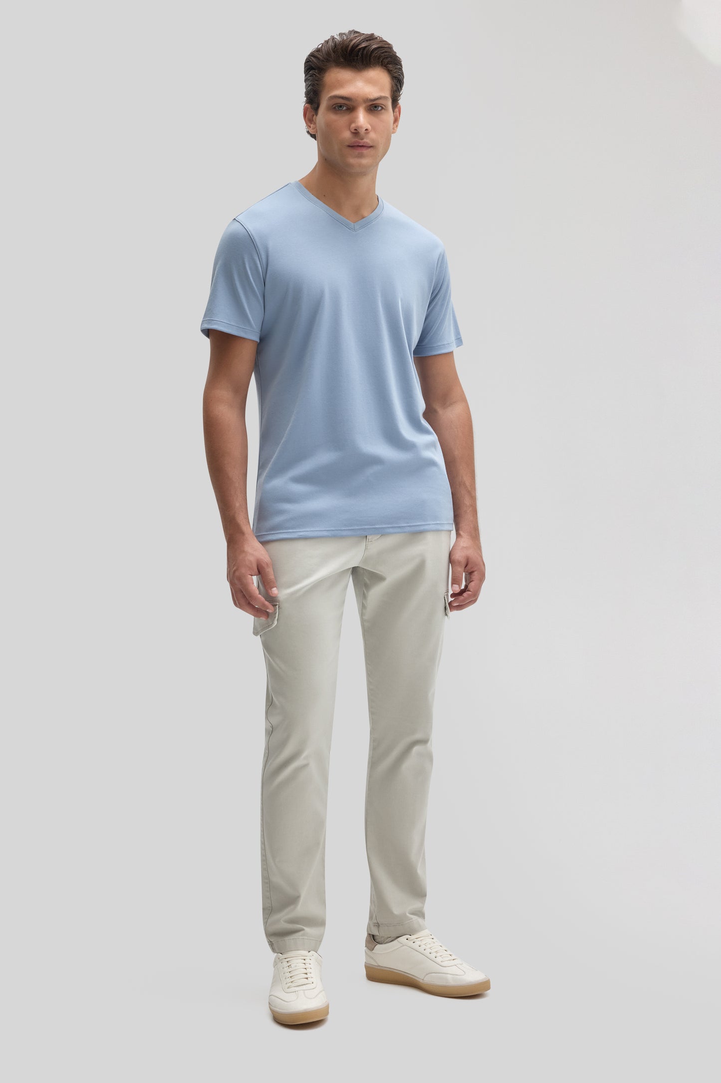 Man wearing light blue V-neck short-sleeve tee with cream pants and white sneakers.