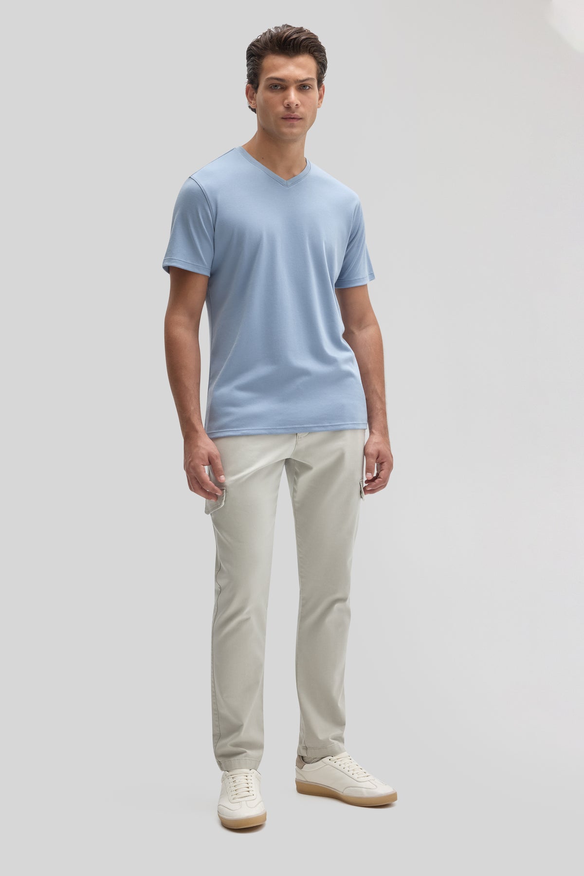 Man wearing light blue V-neck short-sleeve tee with cream pants and white sneakers.