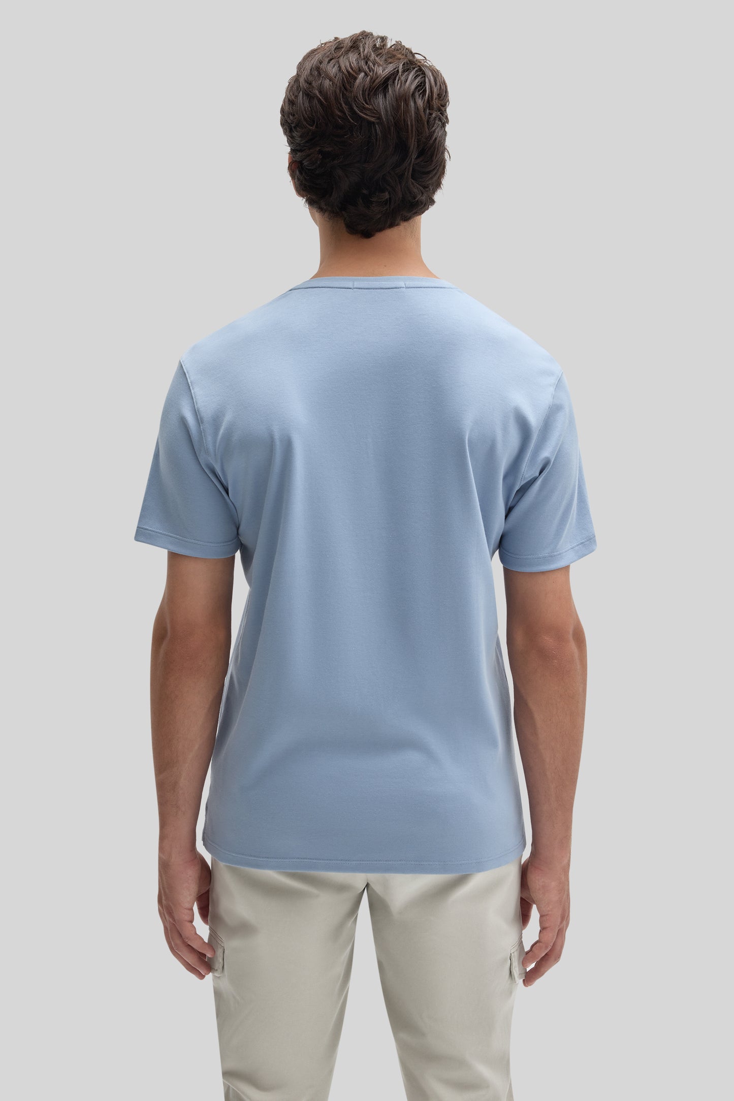 Man wearing light blue V-neck t-shirt with short sleeves and beige cargo pants, shown from behind.