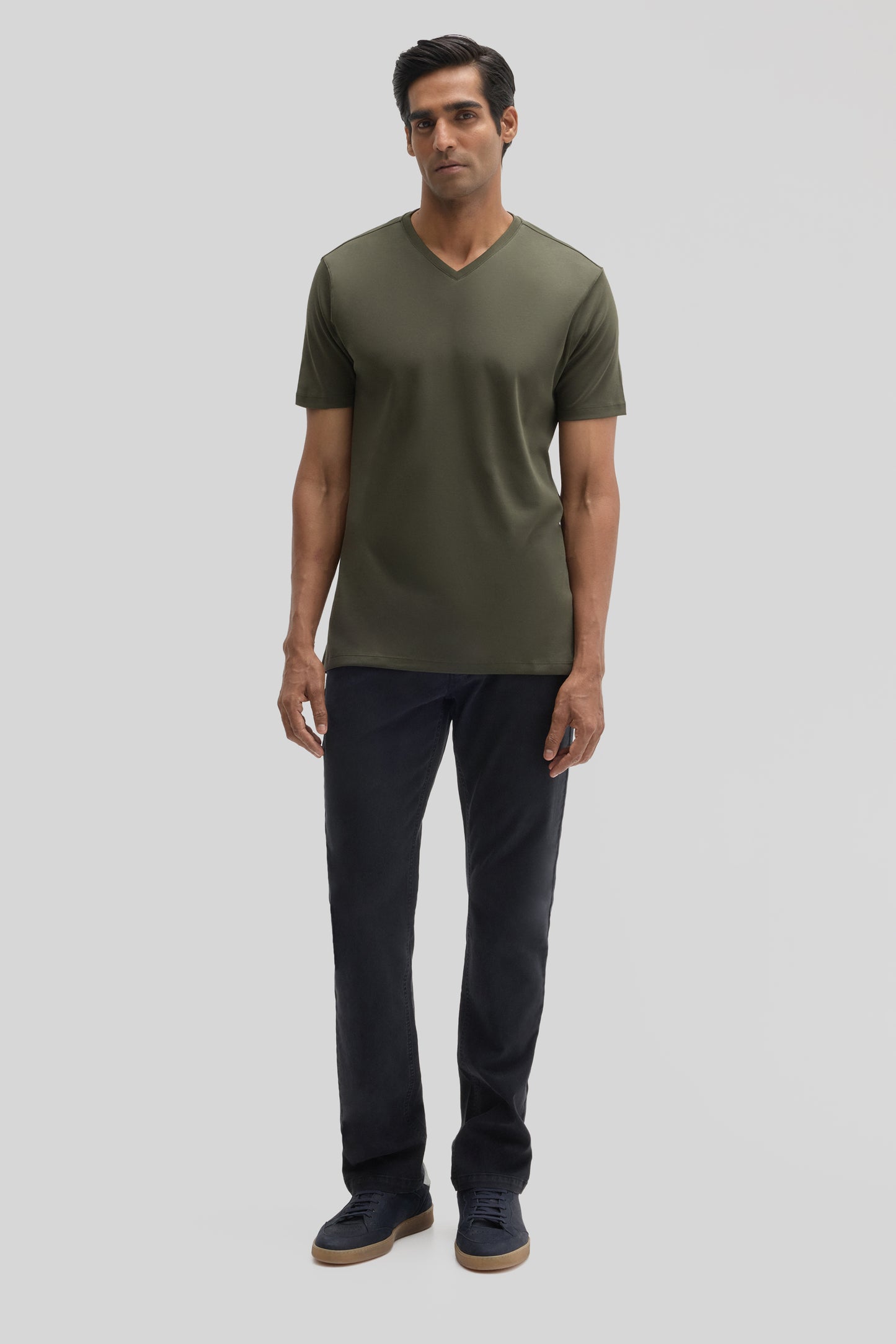 Man wearing olive green V-neck short-sleeve tee with dark navy pants and navy sneakers.