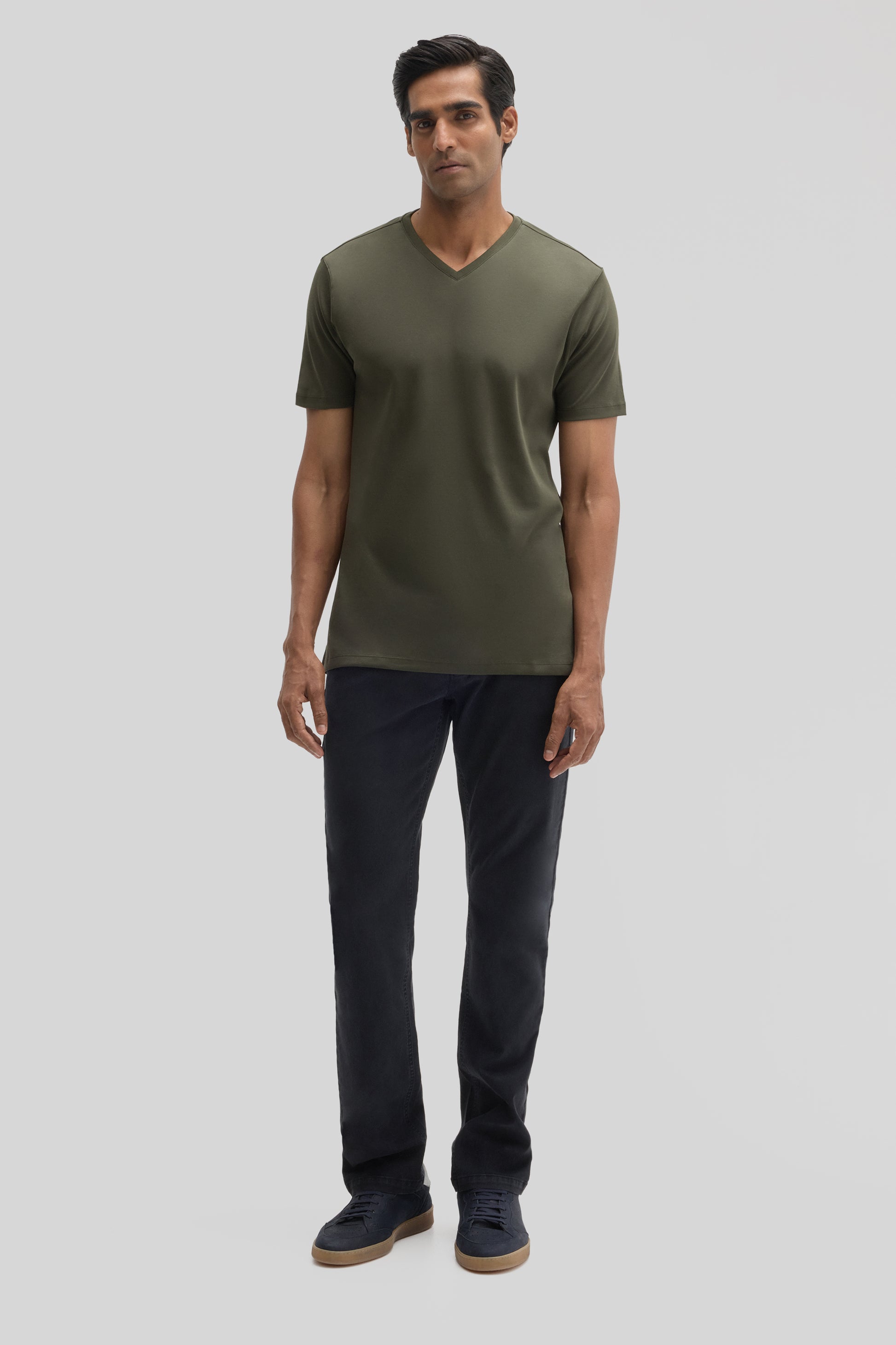 Man wearing olive green V-neck short-sleeve tee with dark navy pants and navy sneakers.