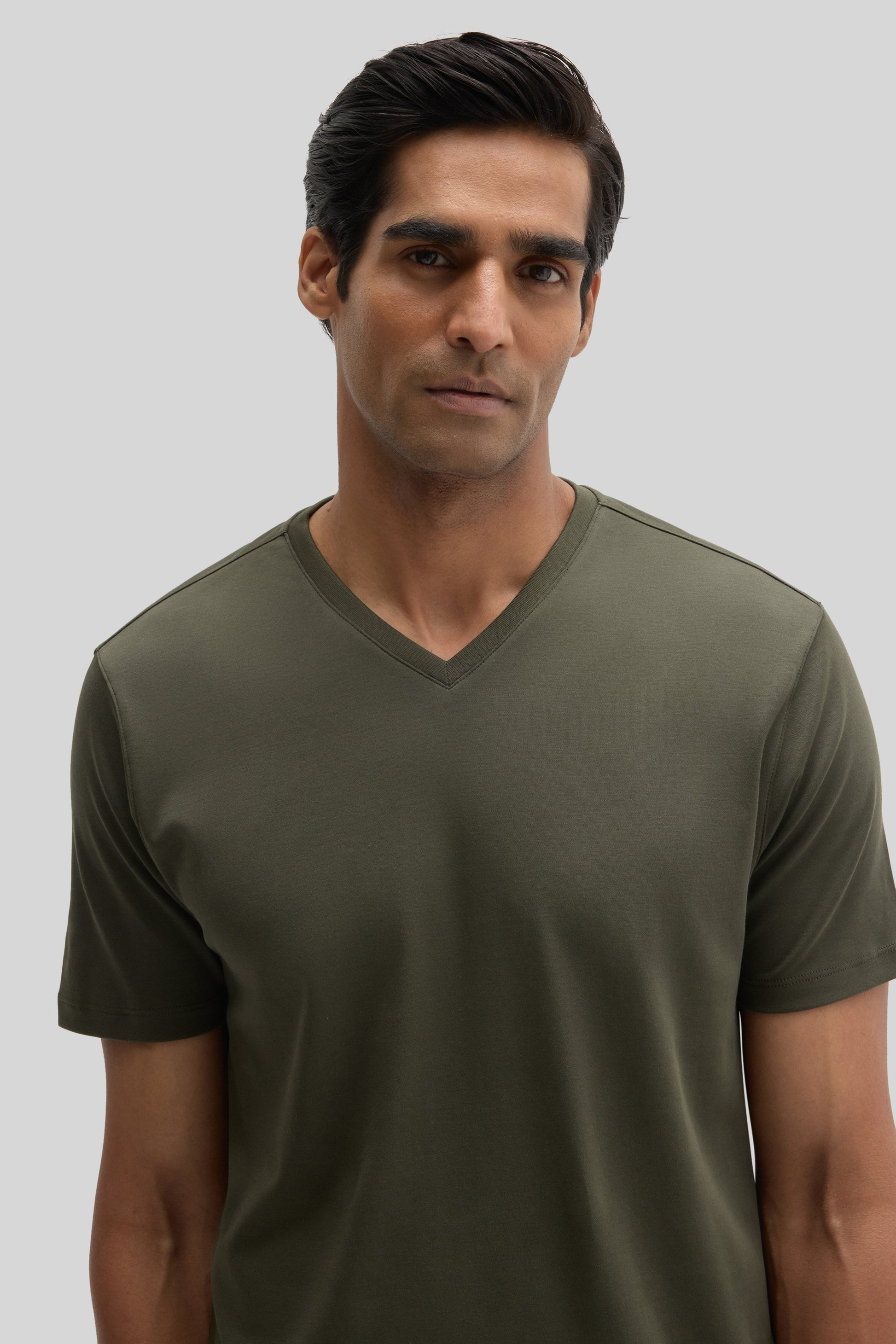Man wearing olive green V-neck short-sleeve t-shirt against neutral background.