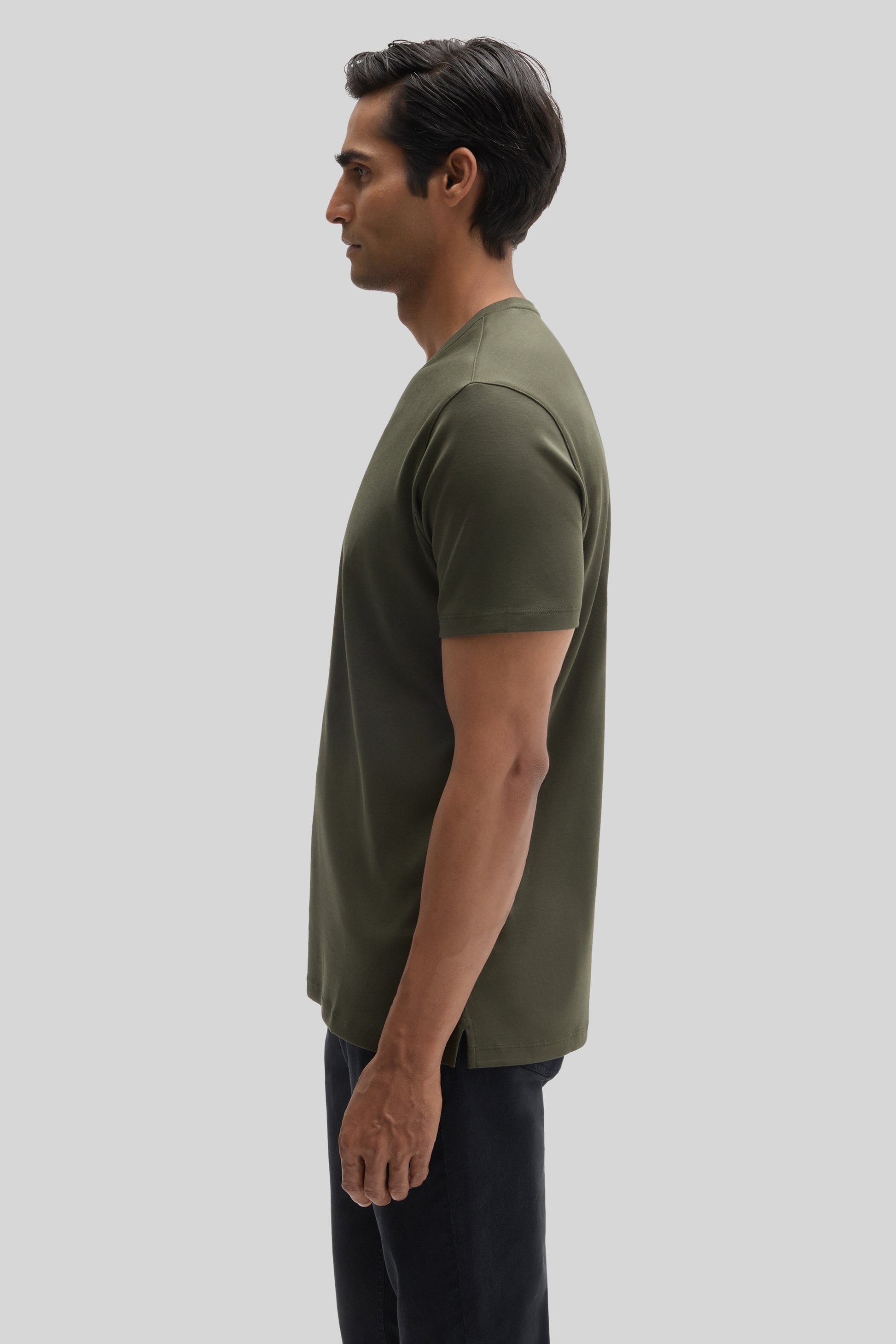 Man wearing olive green V-neck t-shirt with short sleeves and dark pants, shown in side profile view.