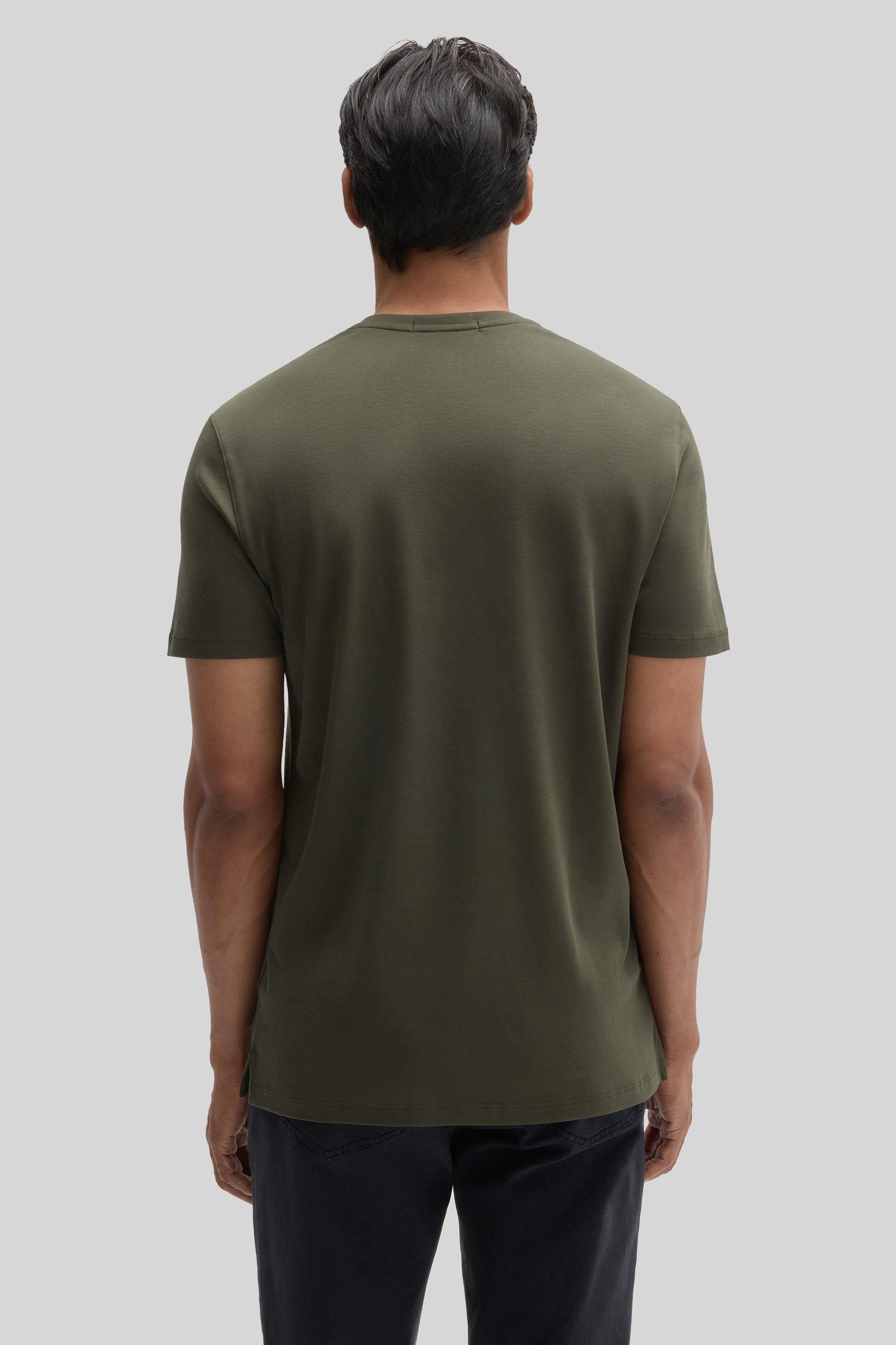 Man wearing olive green V-neck short-sleeve tee, back view, with dark pants.