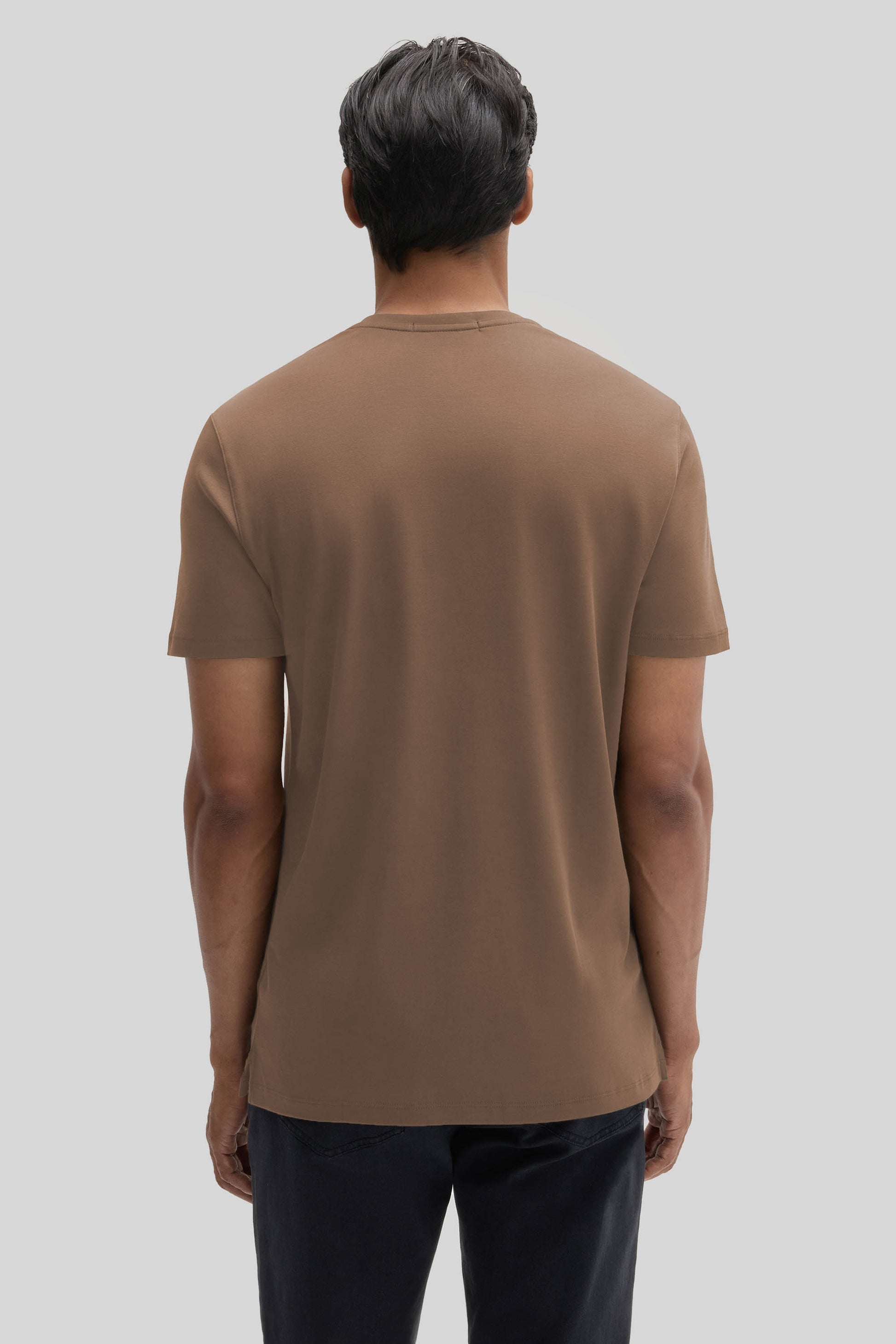 Man wearing tan V-neck t-shirt with short sleeves and dark pants, shown from back view.