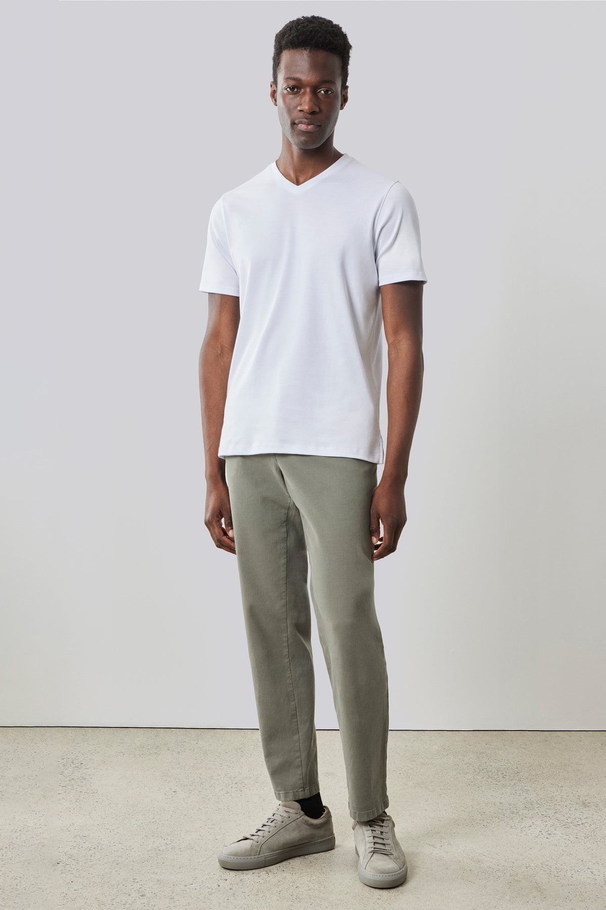 White V-neck short-sleeve t-shirt worn with sage green pants and beige sneakers.