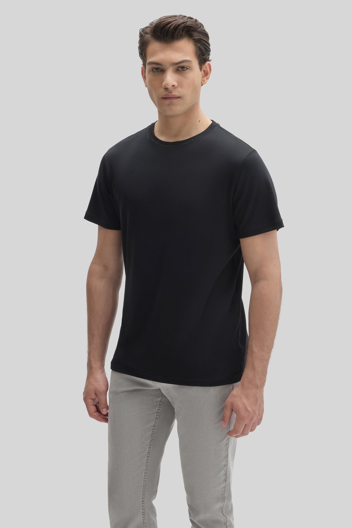 Man wearing a black short-sleeve crew neck t-shirt with gray jeans against a neutral background.