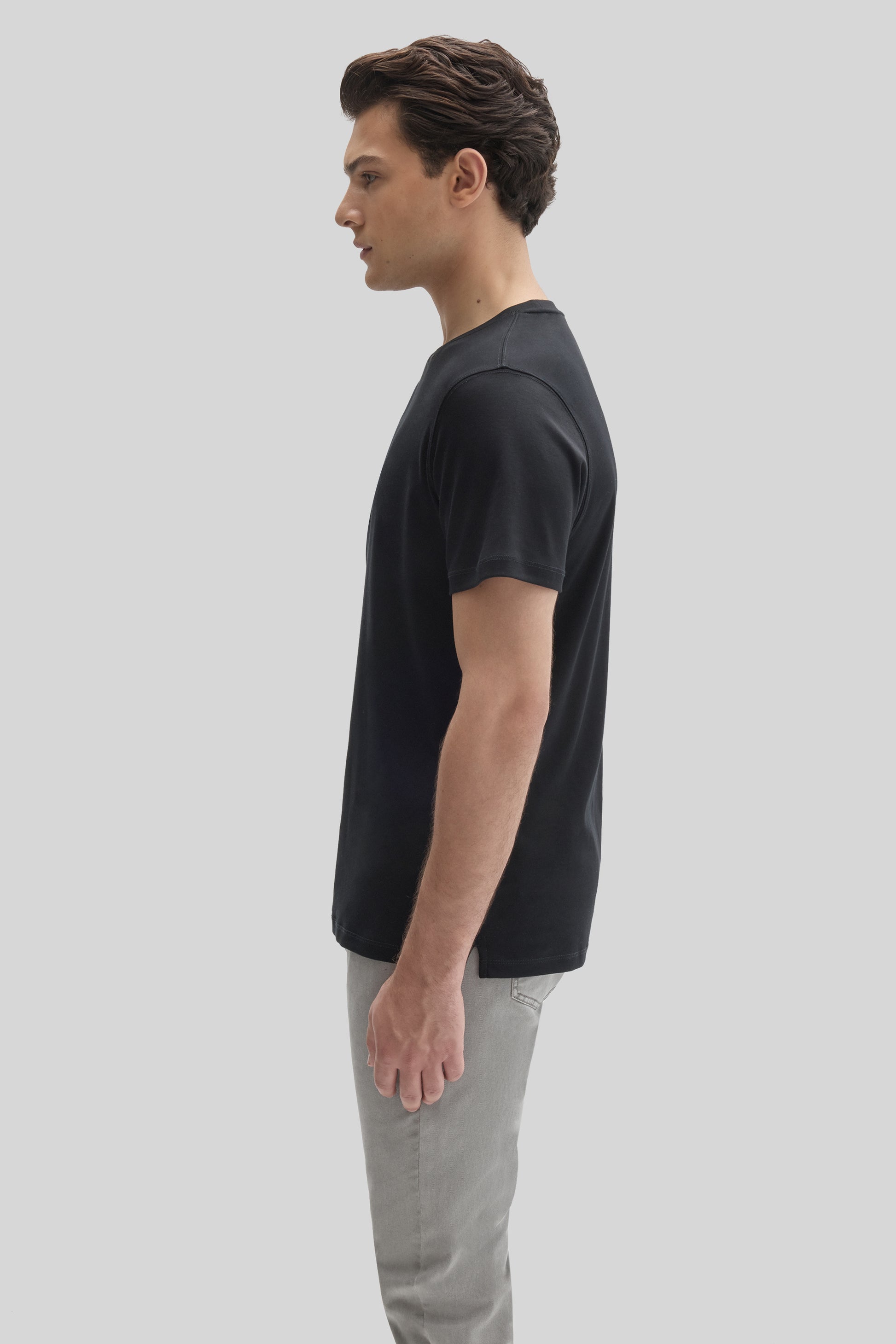 Man wearing black short-sleeve t-shirt with gray pants, shown in side profile.