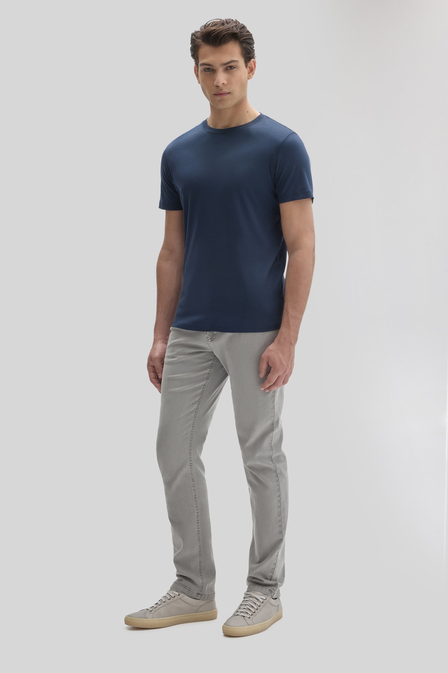 Man wearing a navy blue short-sleeve crew neck tee with gray jeans and light gray sneakers.