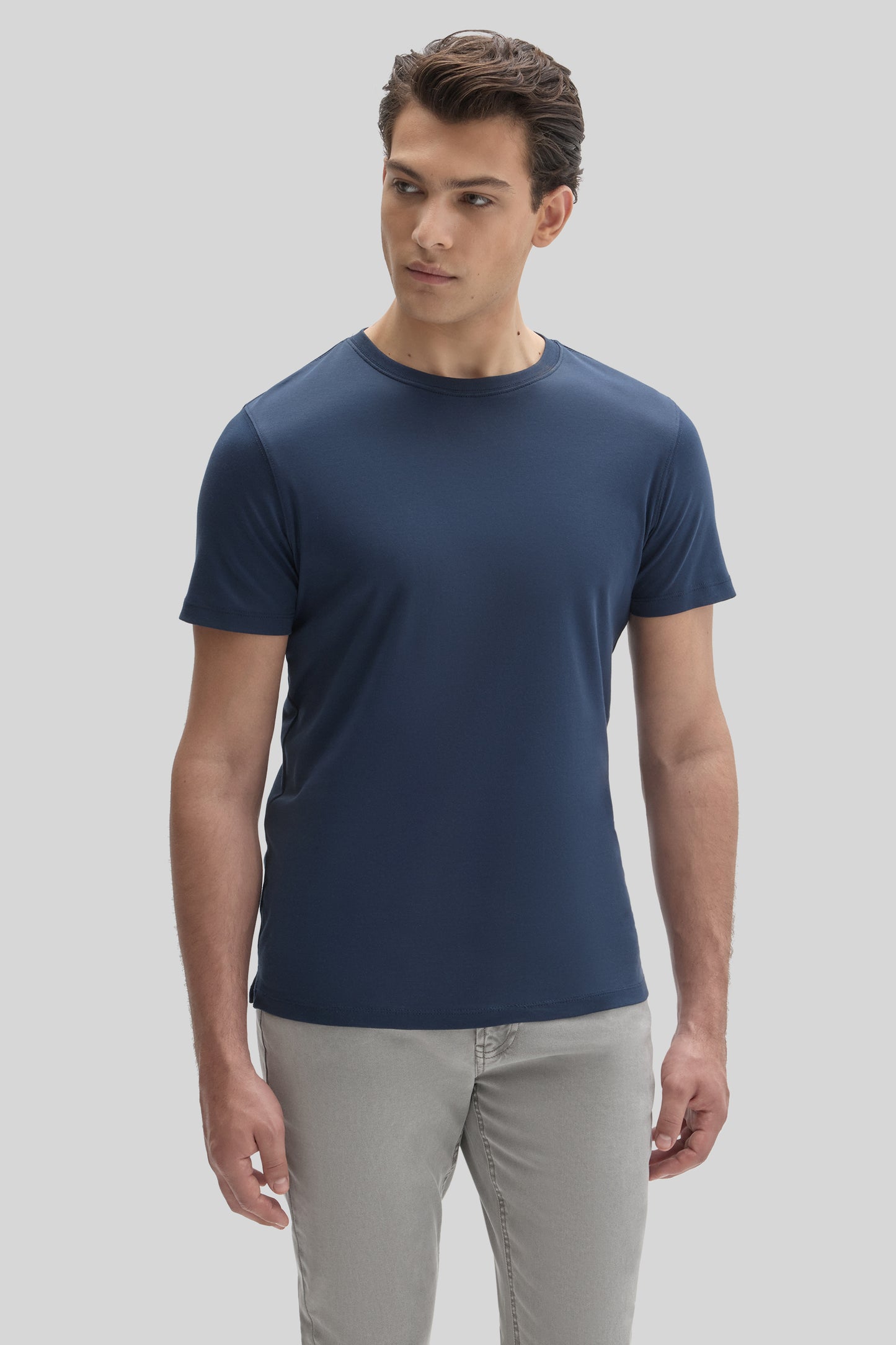 Man wearing dark blue crew-neck short-sleeve tee with gray pants against light gray background.