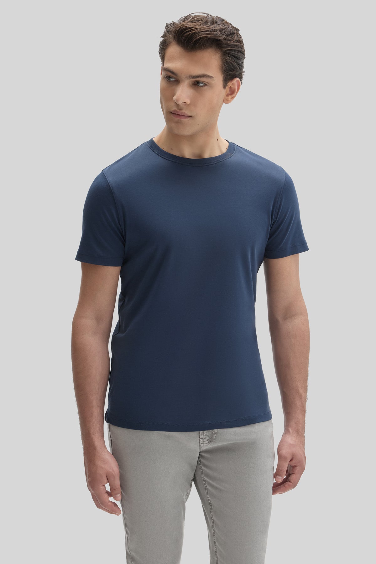 Man wearing dark blue crew-neck short-sleeve tee with gray pants against light gray background.