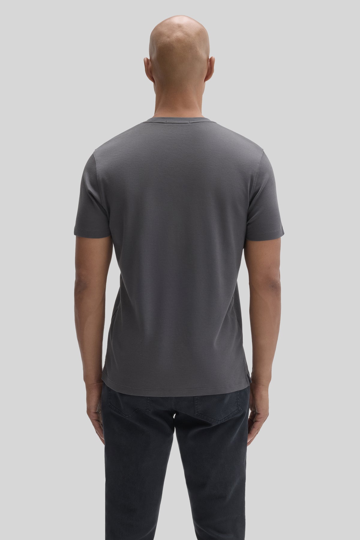 Man wearing charcoal gray short-sleeve t-shirt and dark jeans, shown from back view.