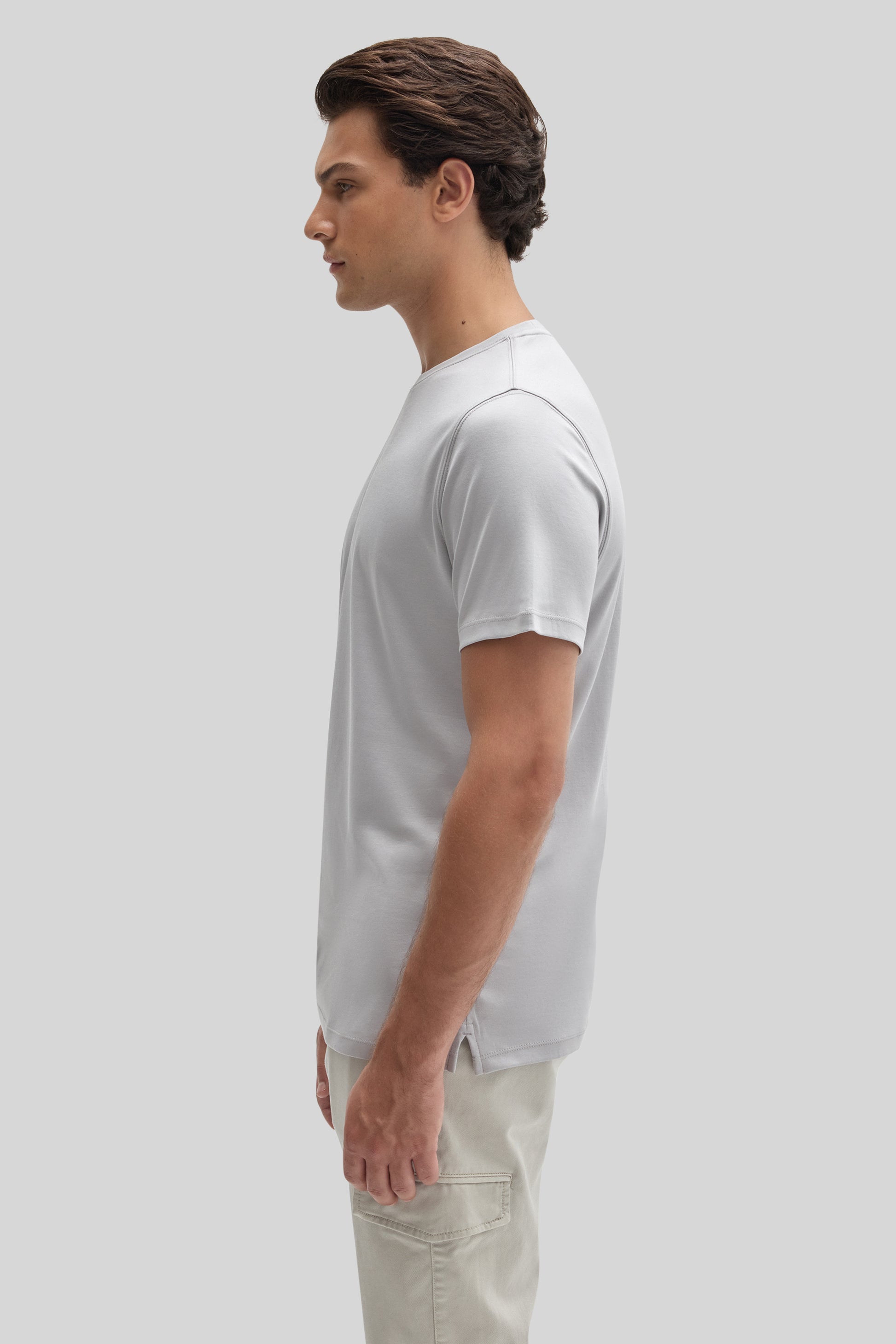 Man wearing white short-sleeve crewneck tee with beige pants, shown in profile view.